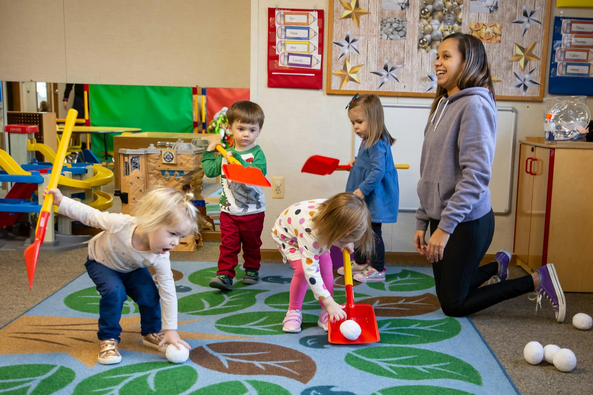Adult and children playing with toy shovels and balls in a classroom