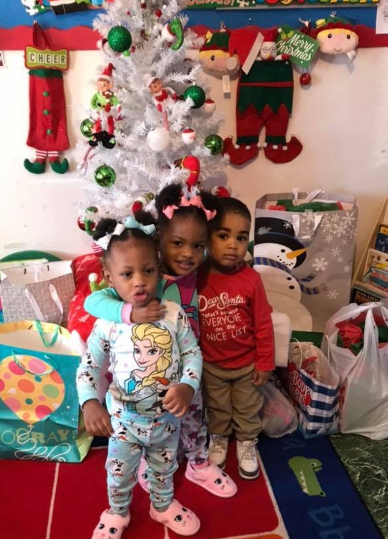 Three children standing in front of a white Christmas tree with gifts