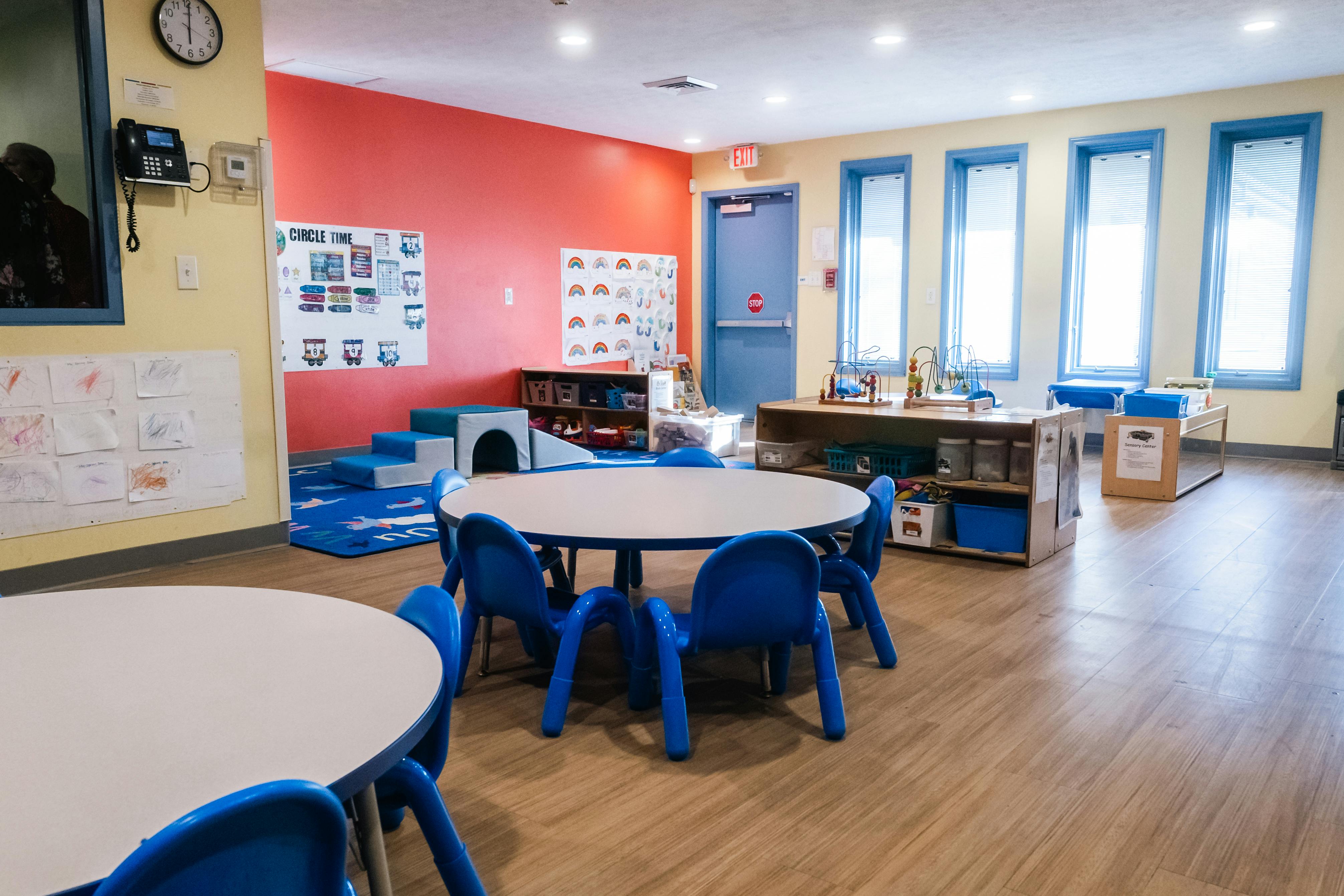 An empty classroom with small tables and chairs, colorful walls, and windows