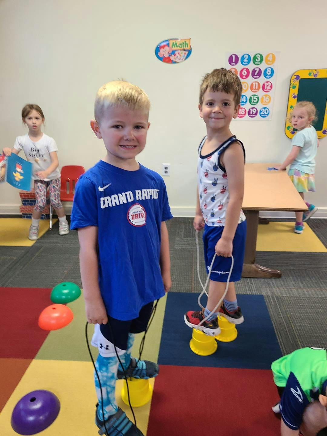 Two children standing on walking stilts in a classroom