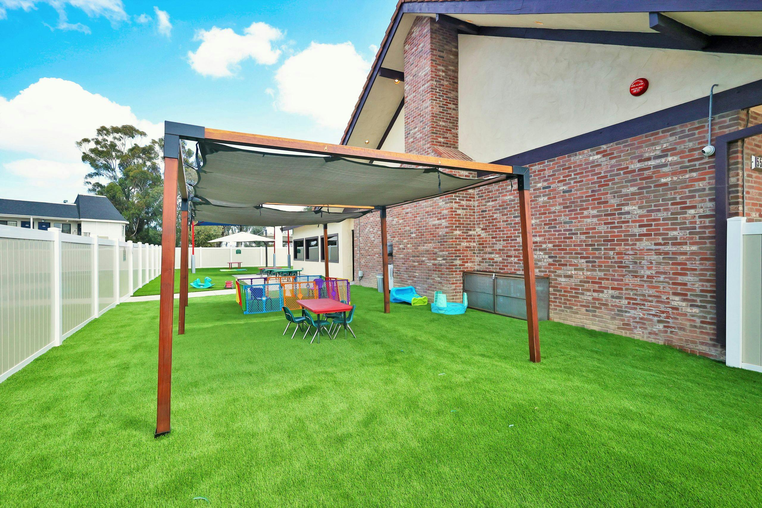 Outdoor play area with artificial turf, a shaded structure, and small colorful furniture