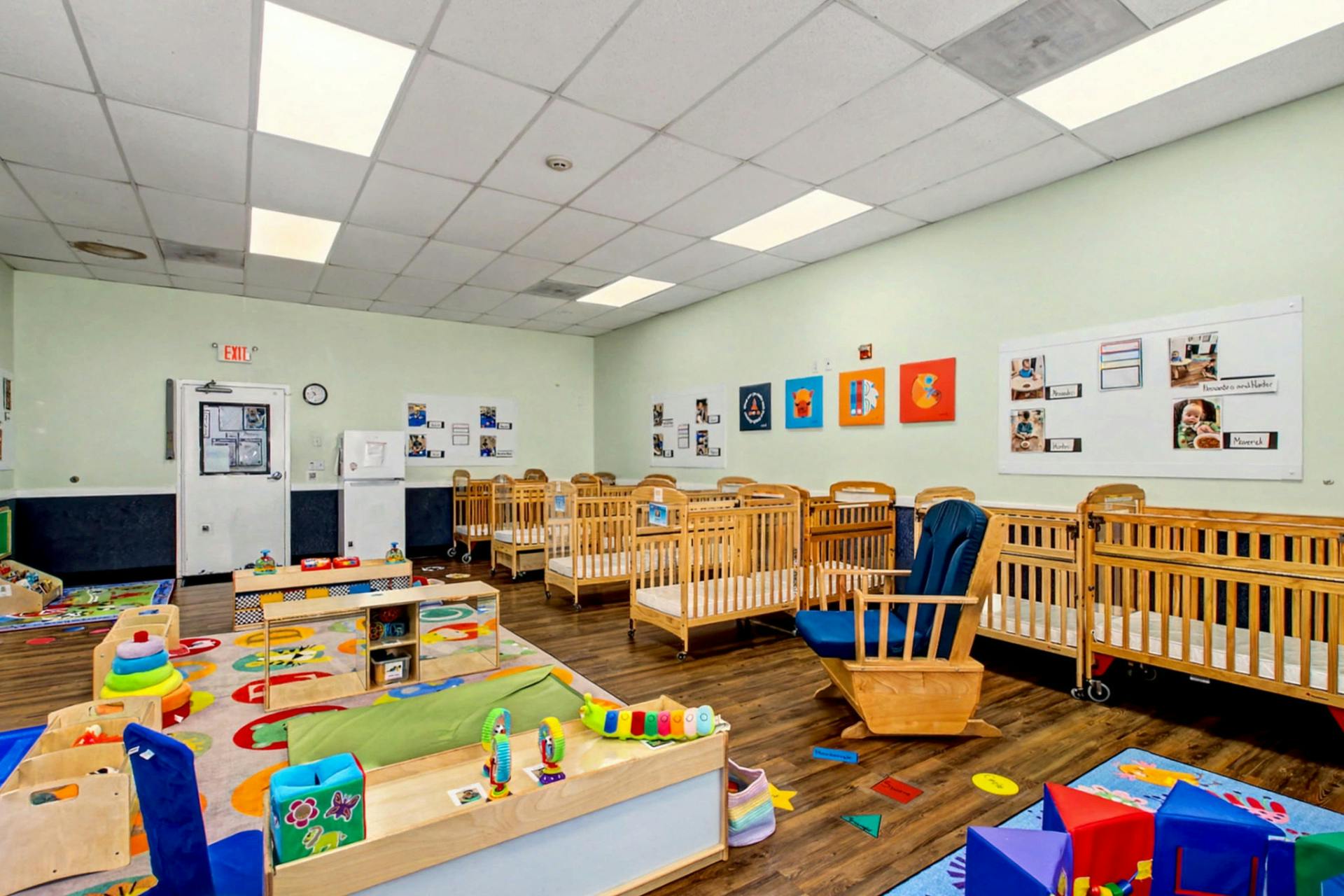 Baby room with multiple cribs, play mats, toys, and a rocking chair