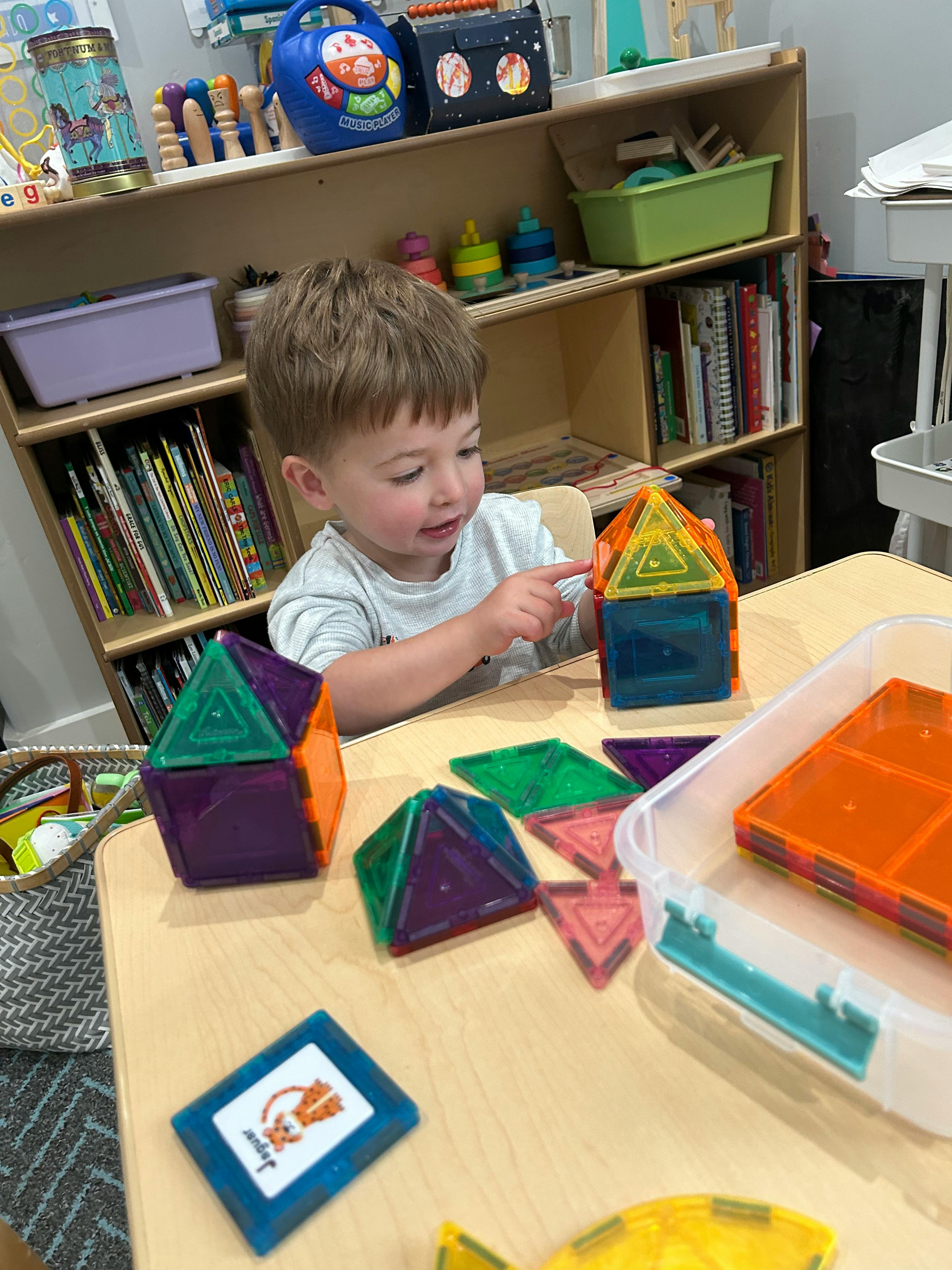 Child playing with colorful magnetic building tiles at a table