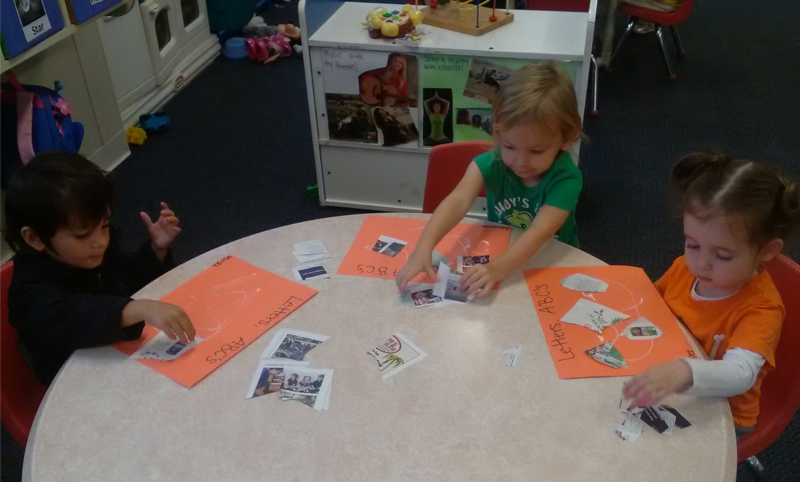 Three children at a table working with paper and small pictures