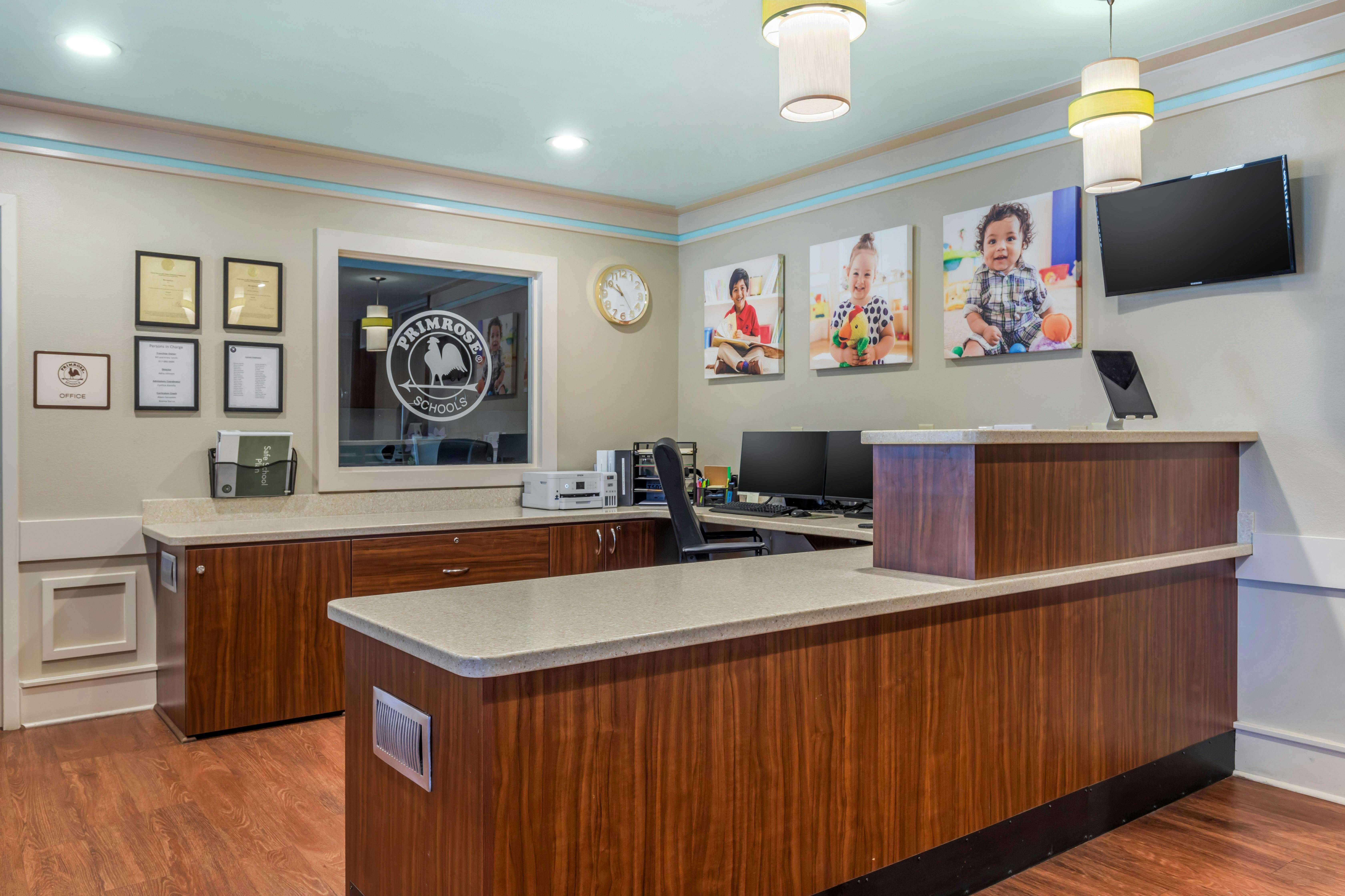 Reception desk with office door, three pictures of children, and a TV screen