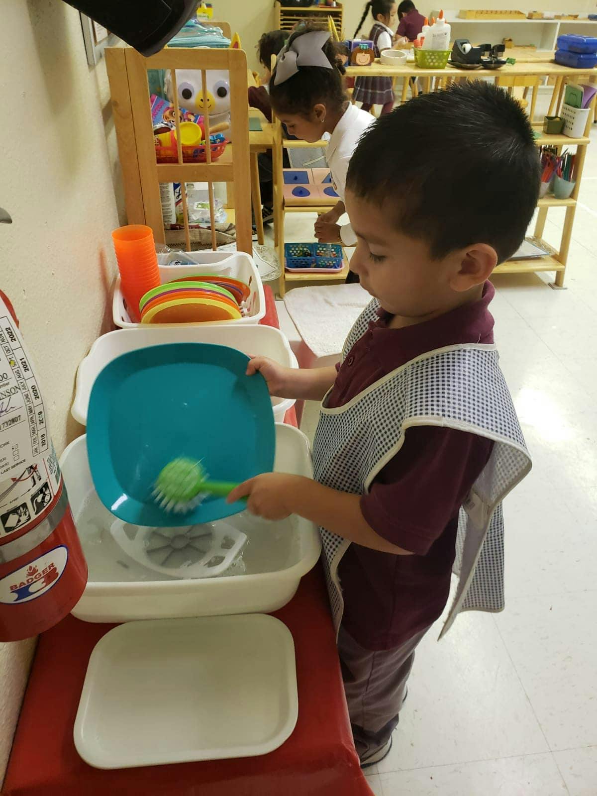 Child washing a blue plate with a brush in a classroom