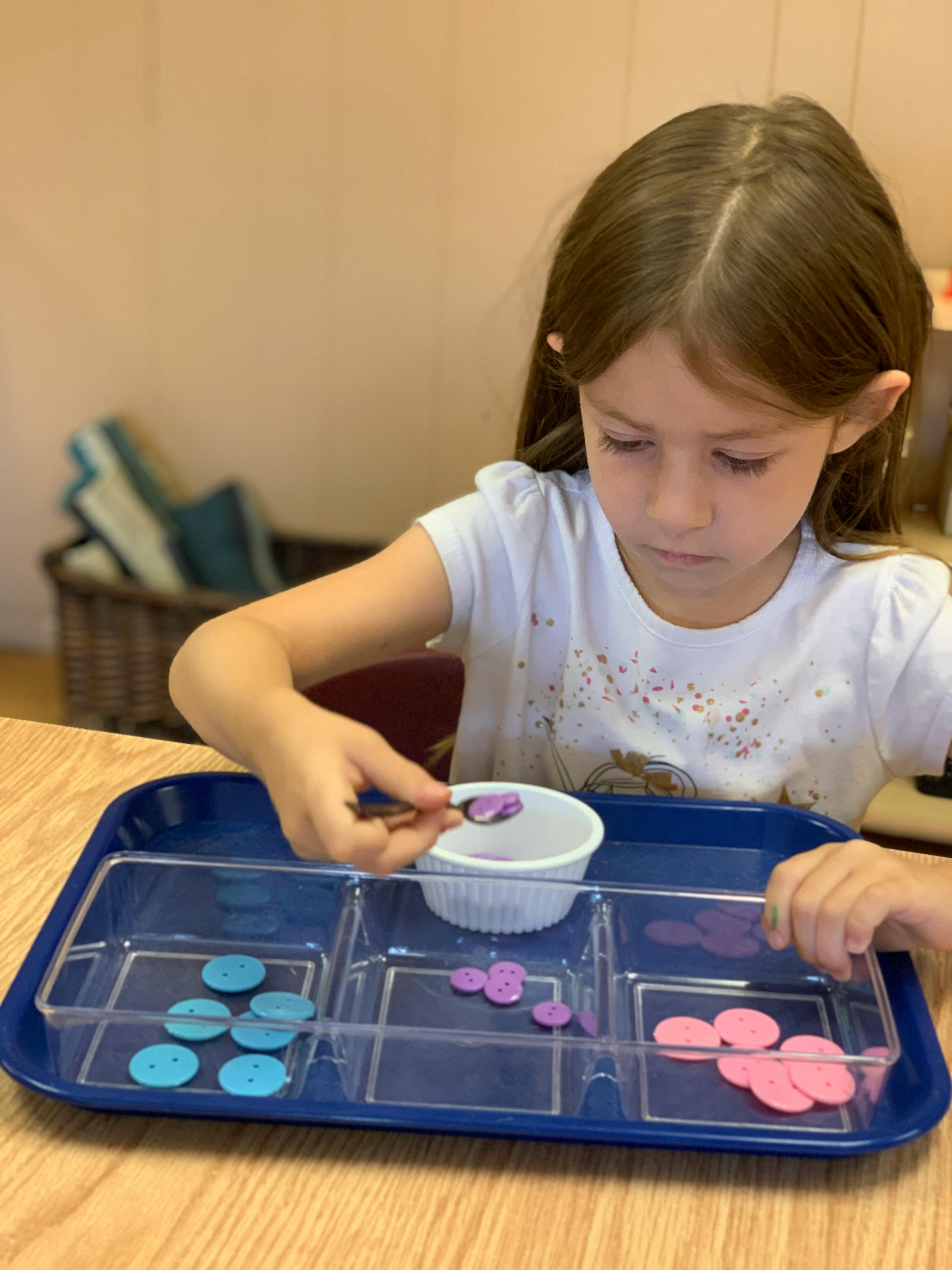 Child using a spoon to move small objects on a tray