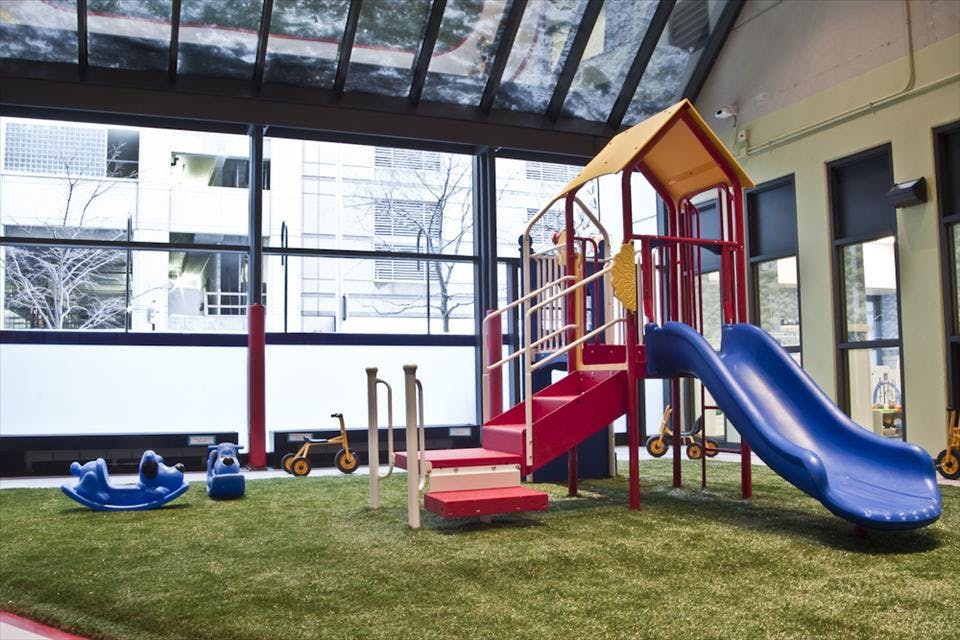 Indoor playground with red and blue slides and a green artificial turf floor