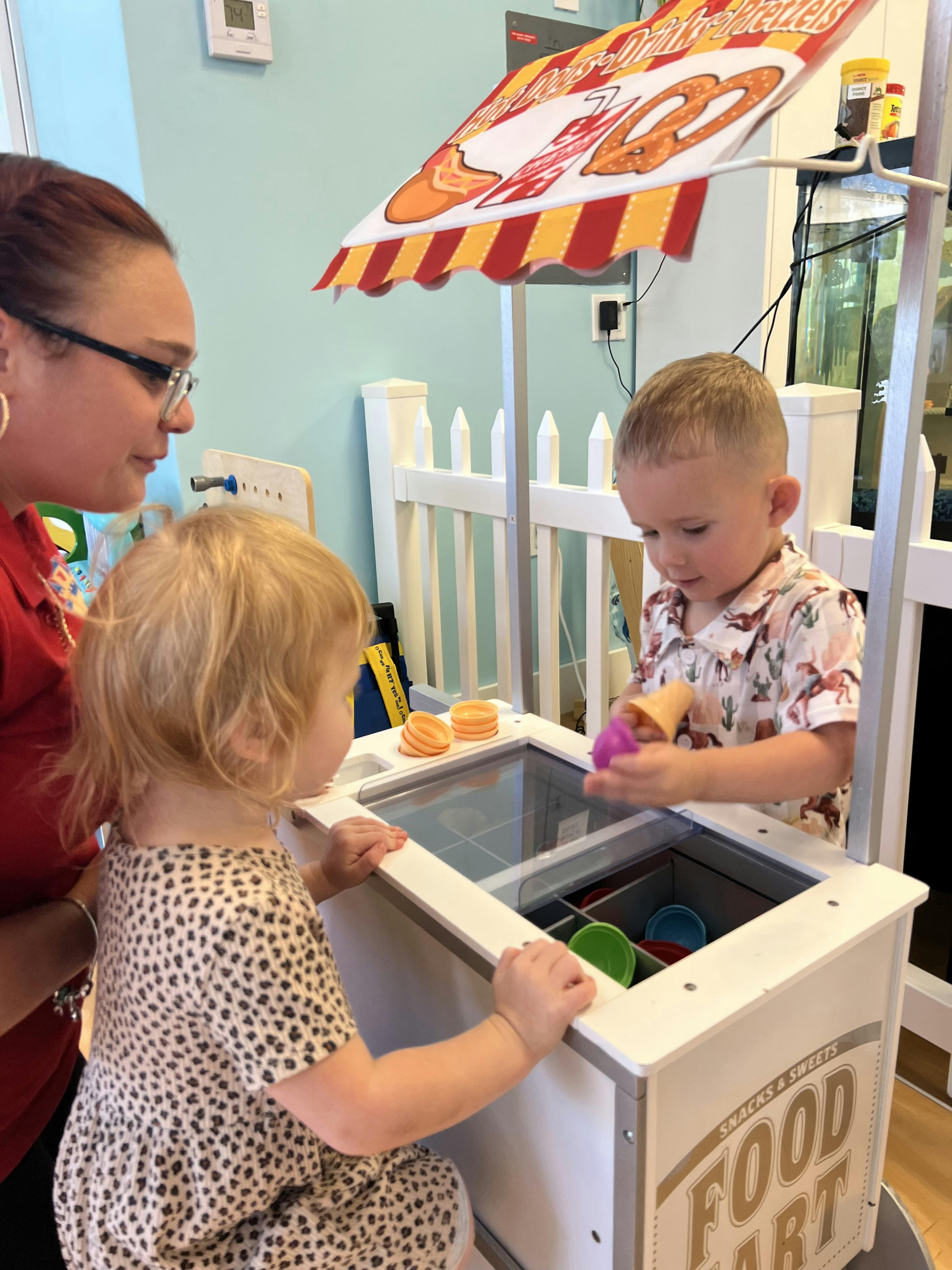 Adult and two children playing with a pretend food cart