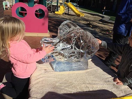 Child touching a large ice sculpture outdoors