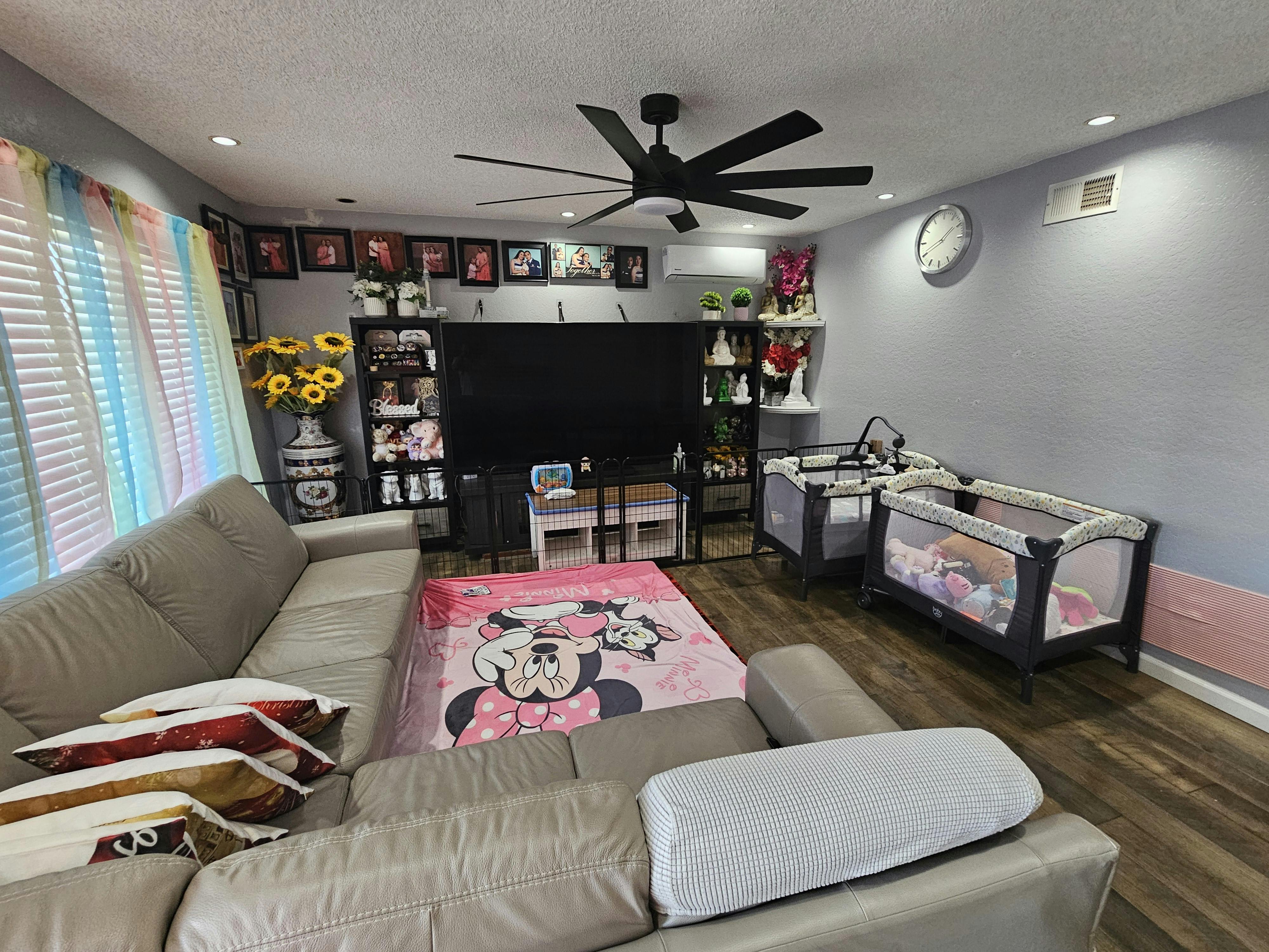 Living room with a large sofa, two baby cribs, and a ceiling fan
