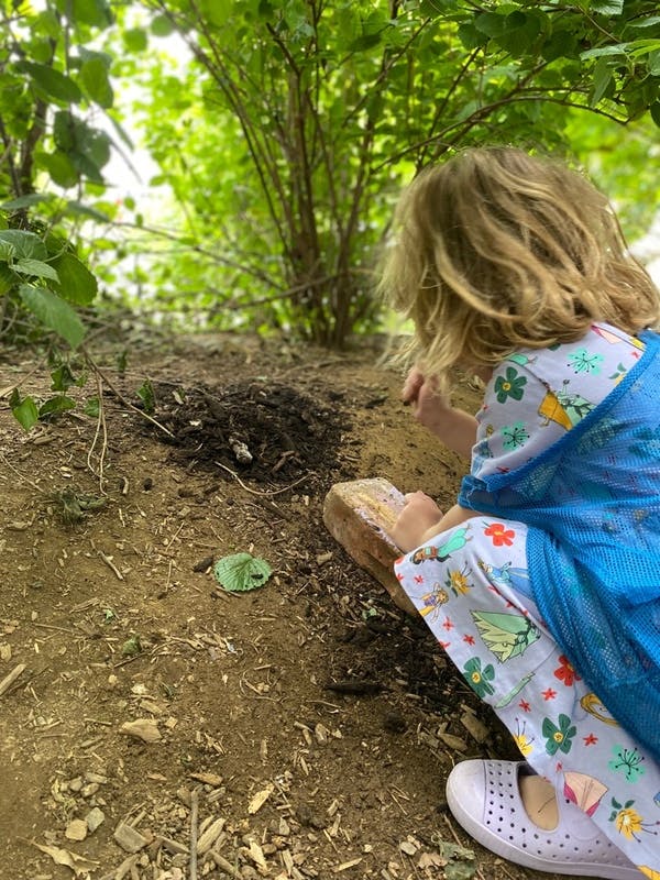 Child kneeling on the ground looking at a small pile of dirt
