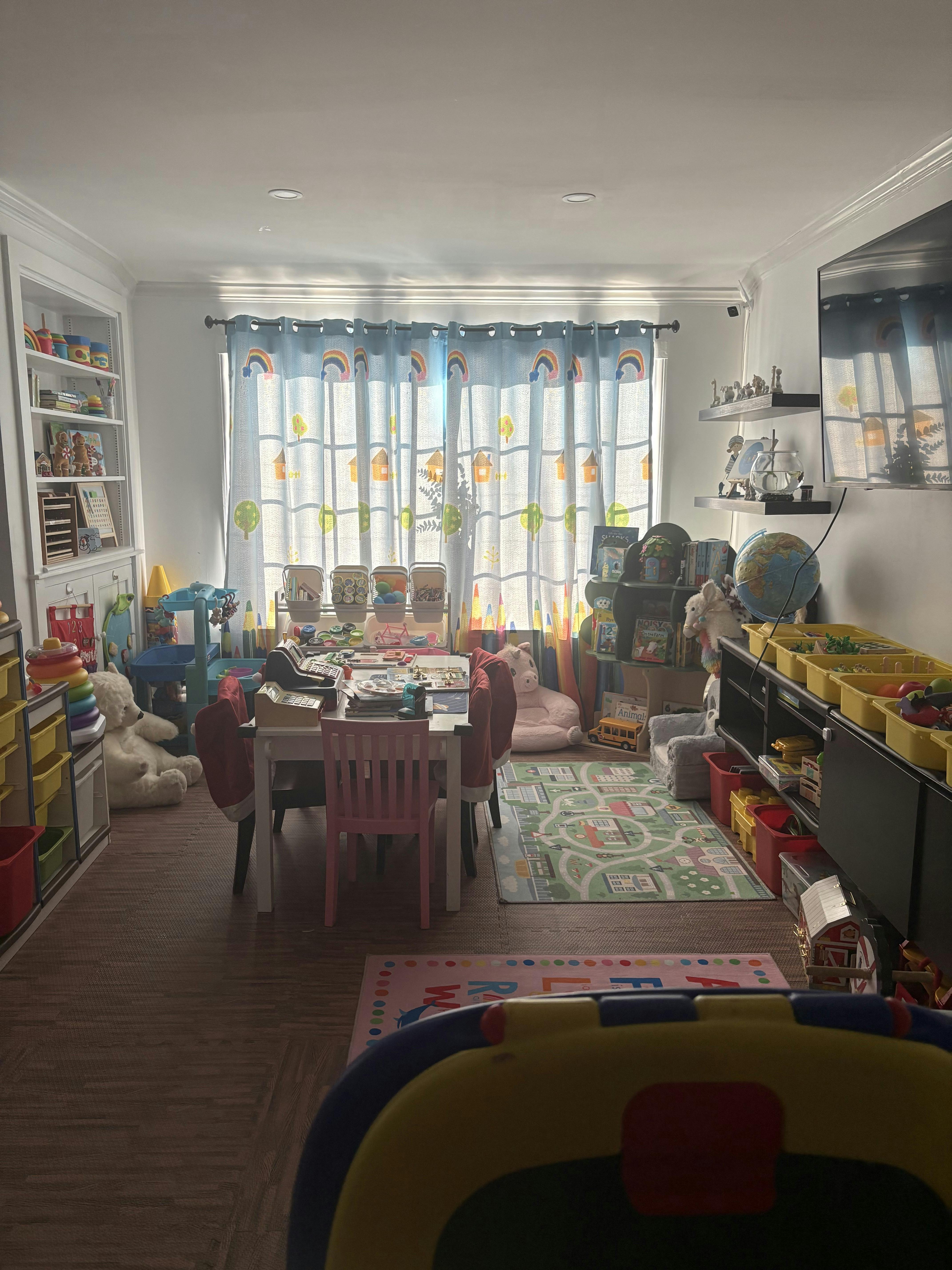 Playroom with a table and chairs, shelves of toys, and rainbow curtains
