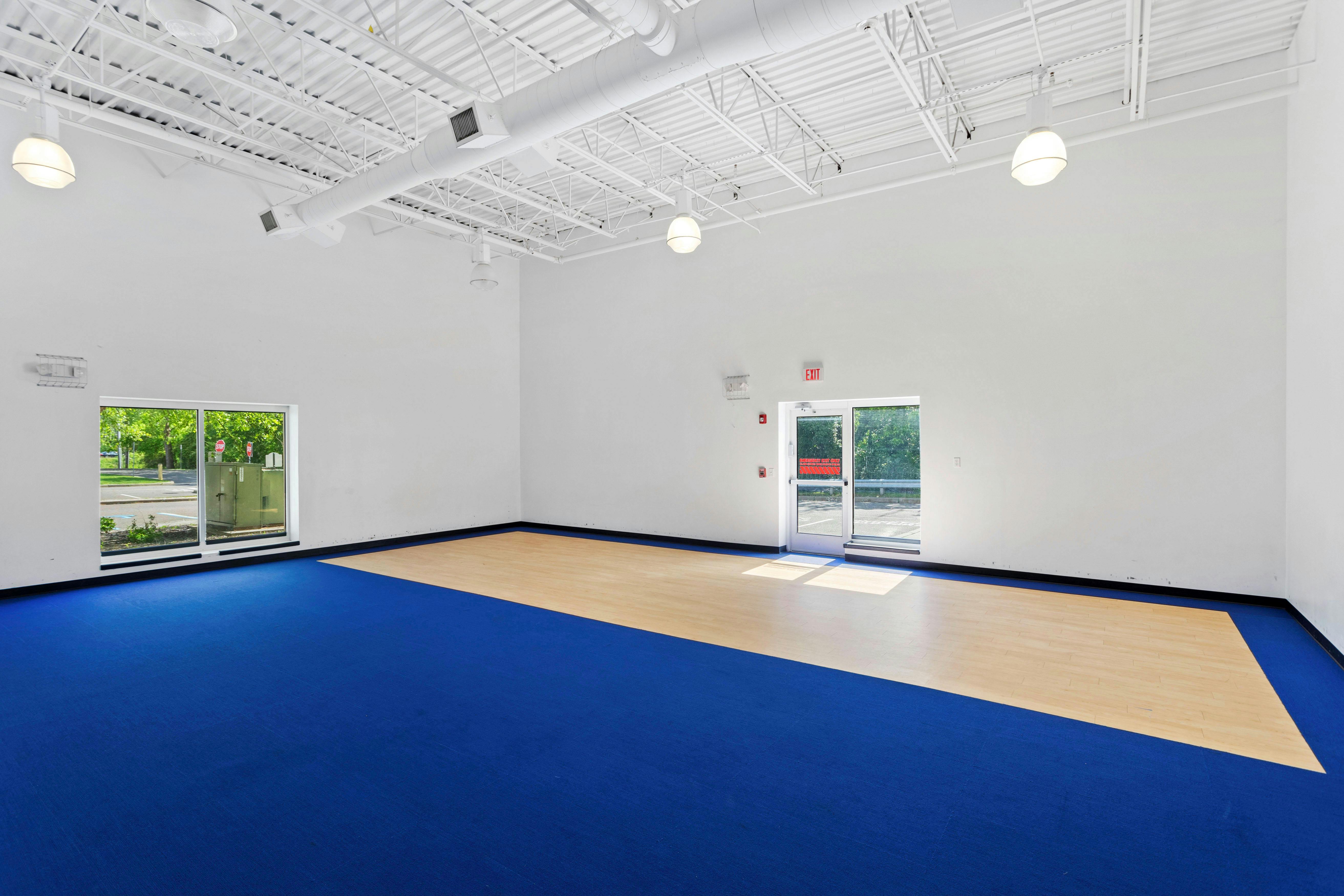 An empty indoor room with blue carpet and a light wood floor section