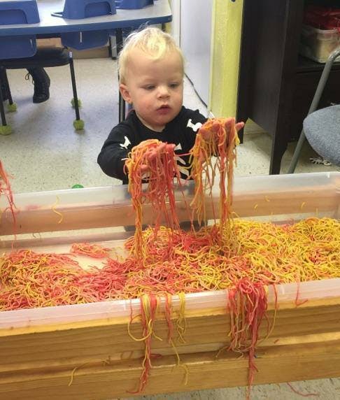 Child playing with colorful noodles in a sensory bin