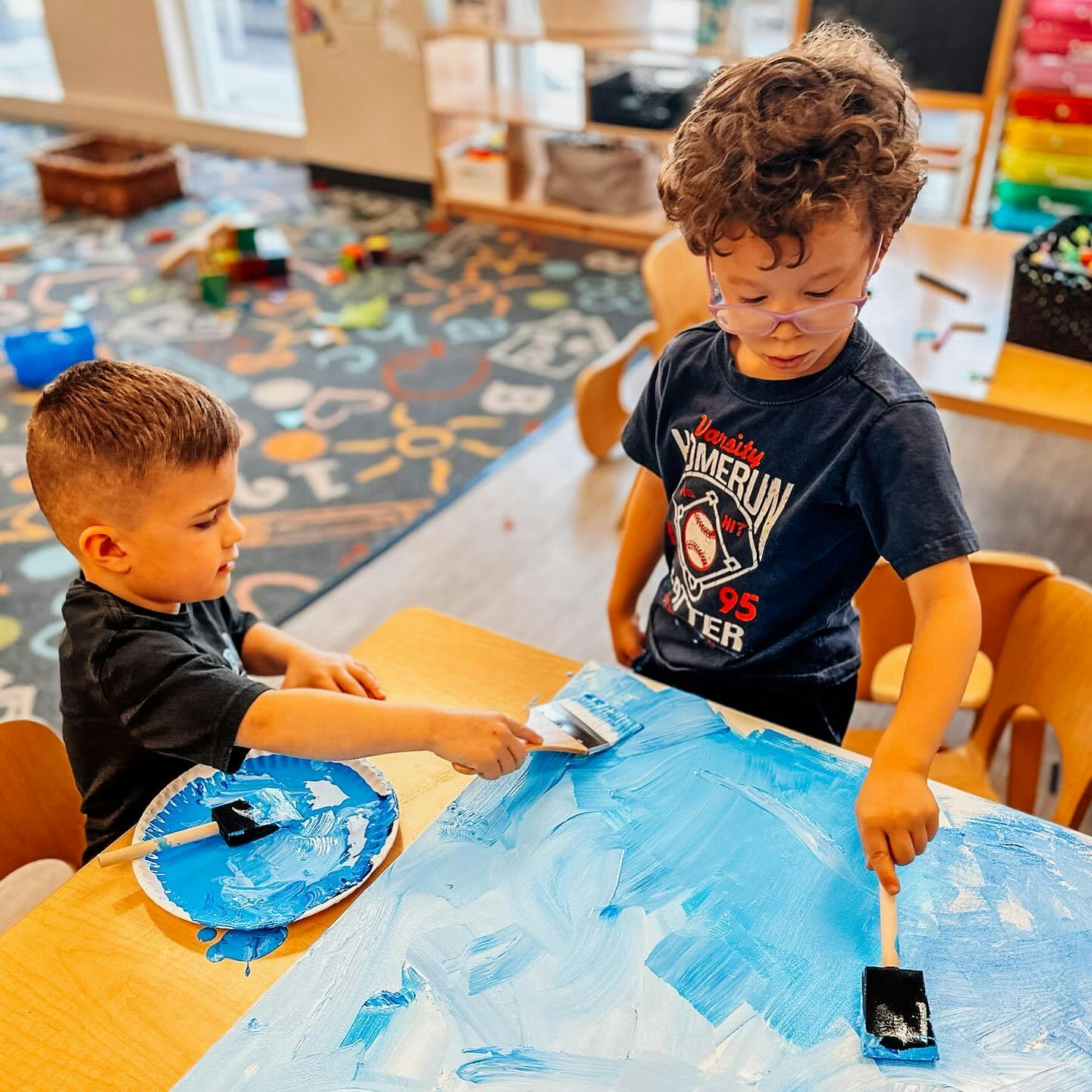 Two children painting with blue paint at a table