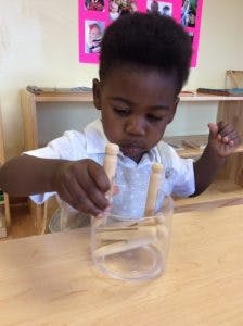Child playing with wooden pegs and a clear container