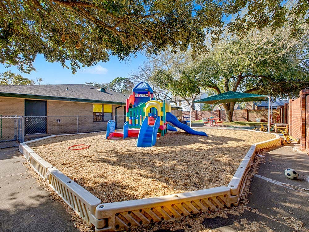 Colorful playground with slides and wood chips surrounded by a low fence