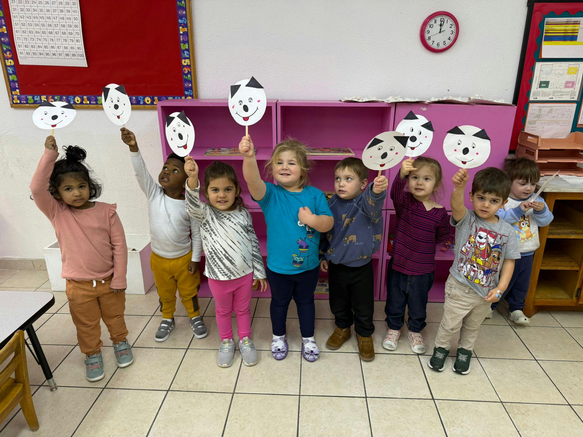 Group of children holding up paper masks in a classroom