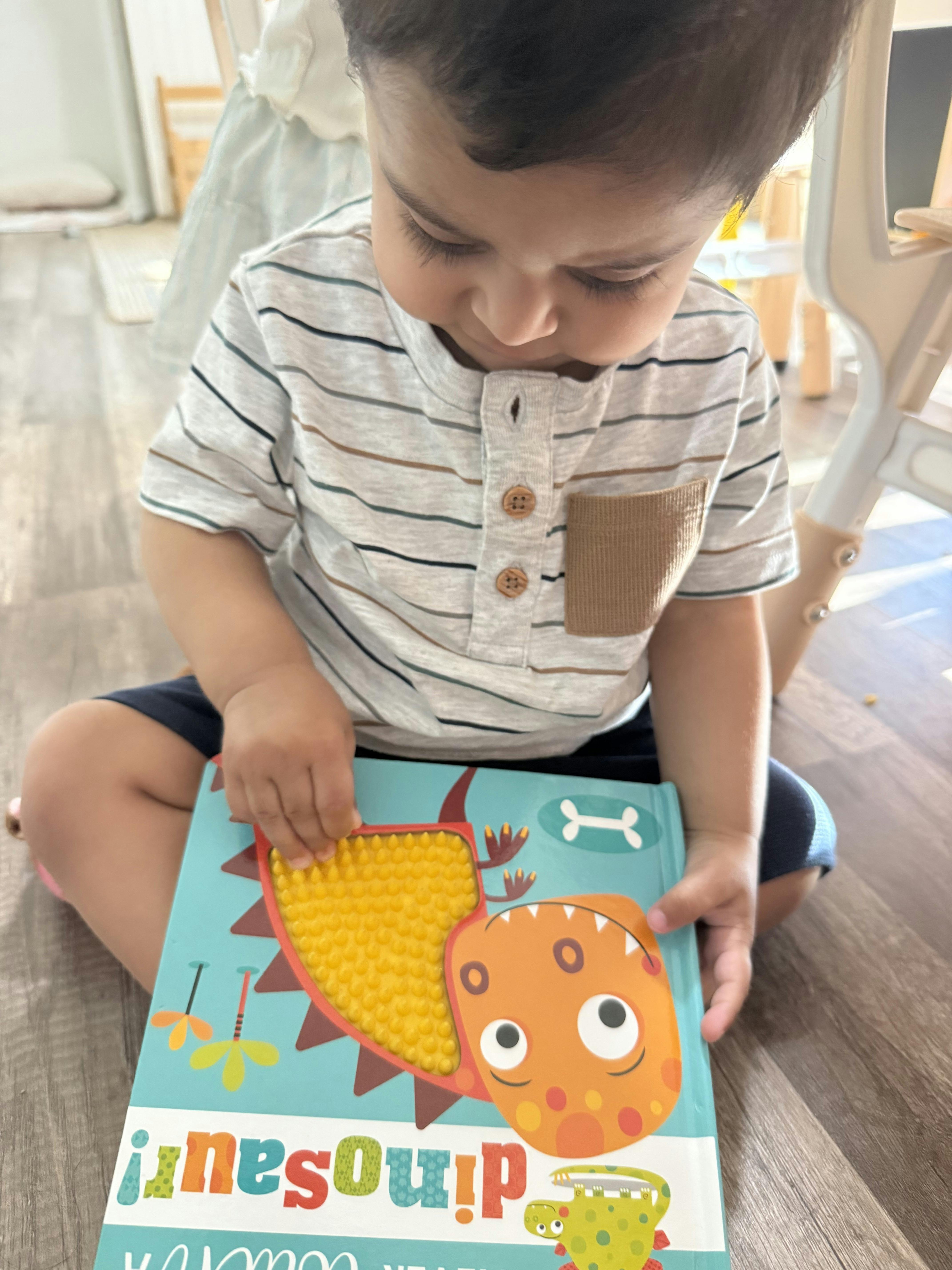 Child touching a textured dinosaur book on the floor