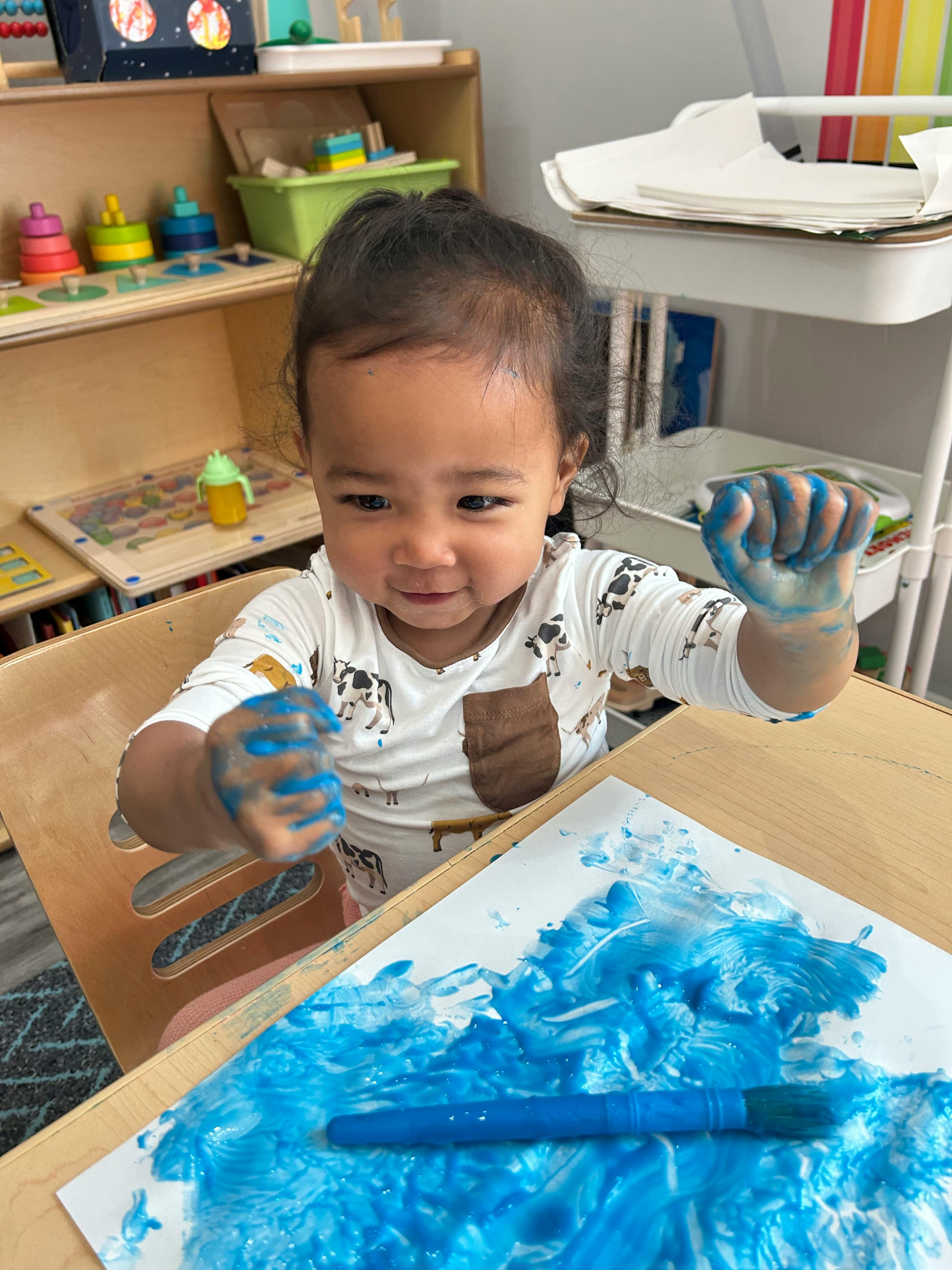 Child with blue paint on hands and paper