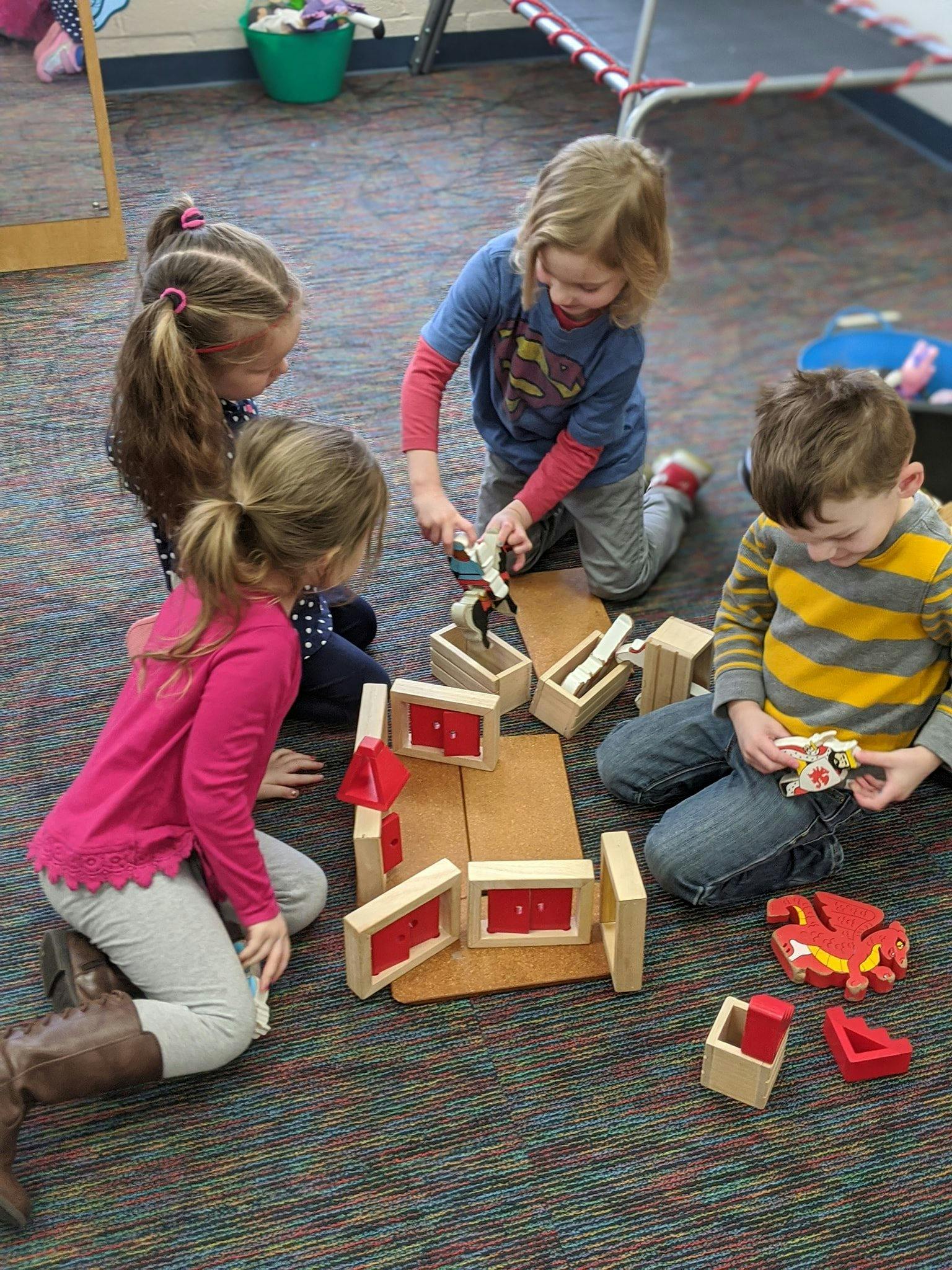 Four children playing with wooden blocks on a carpeted floor