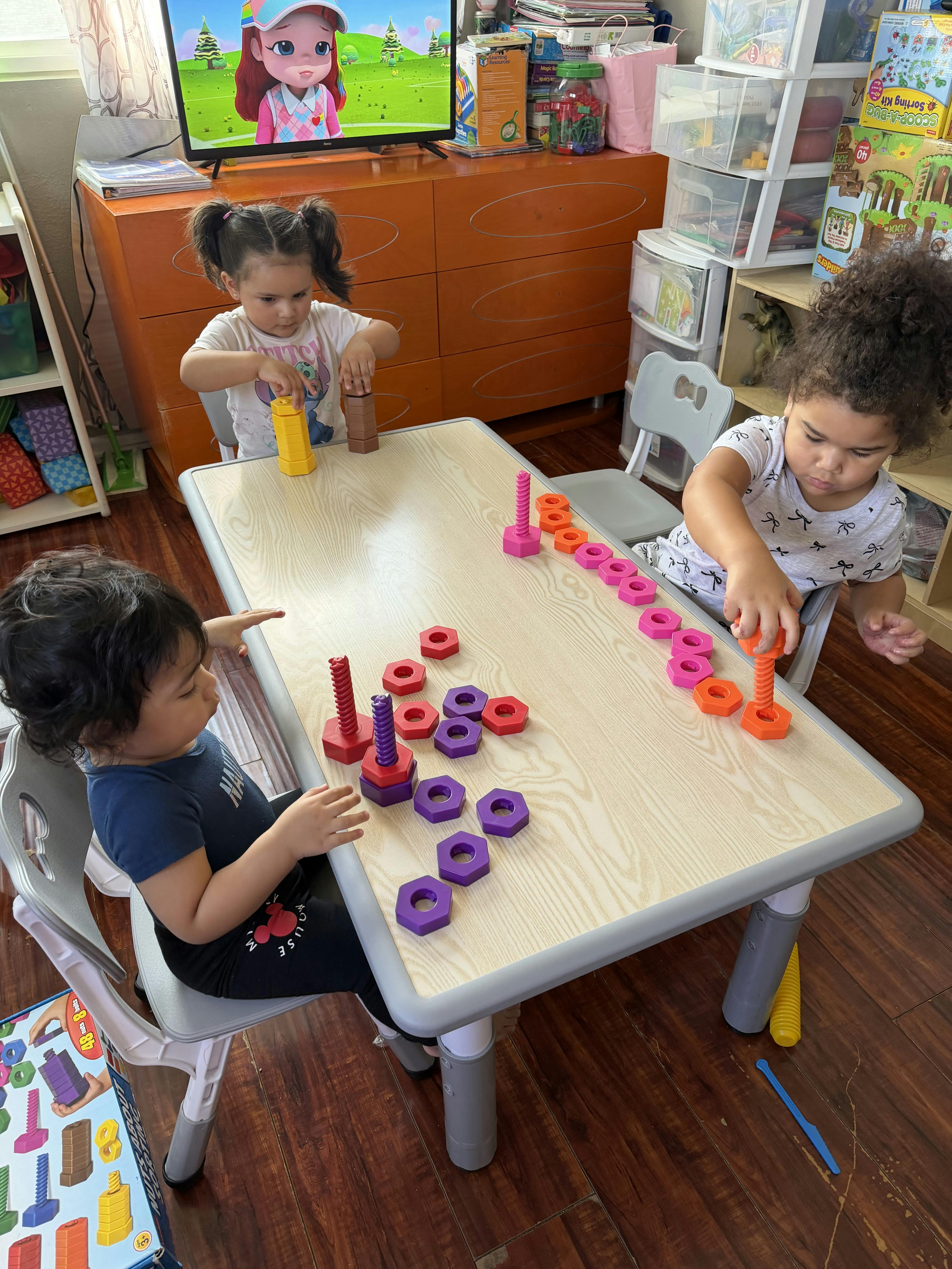 Three children playing with colorful nuts and bolts on a table