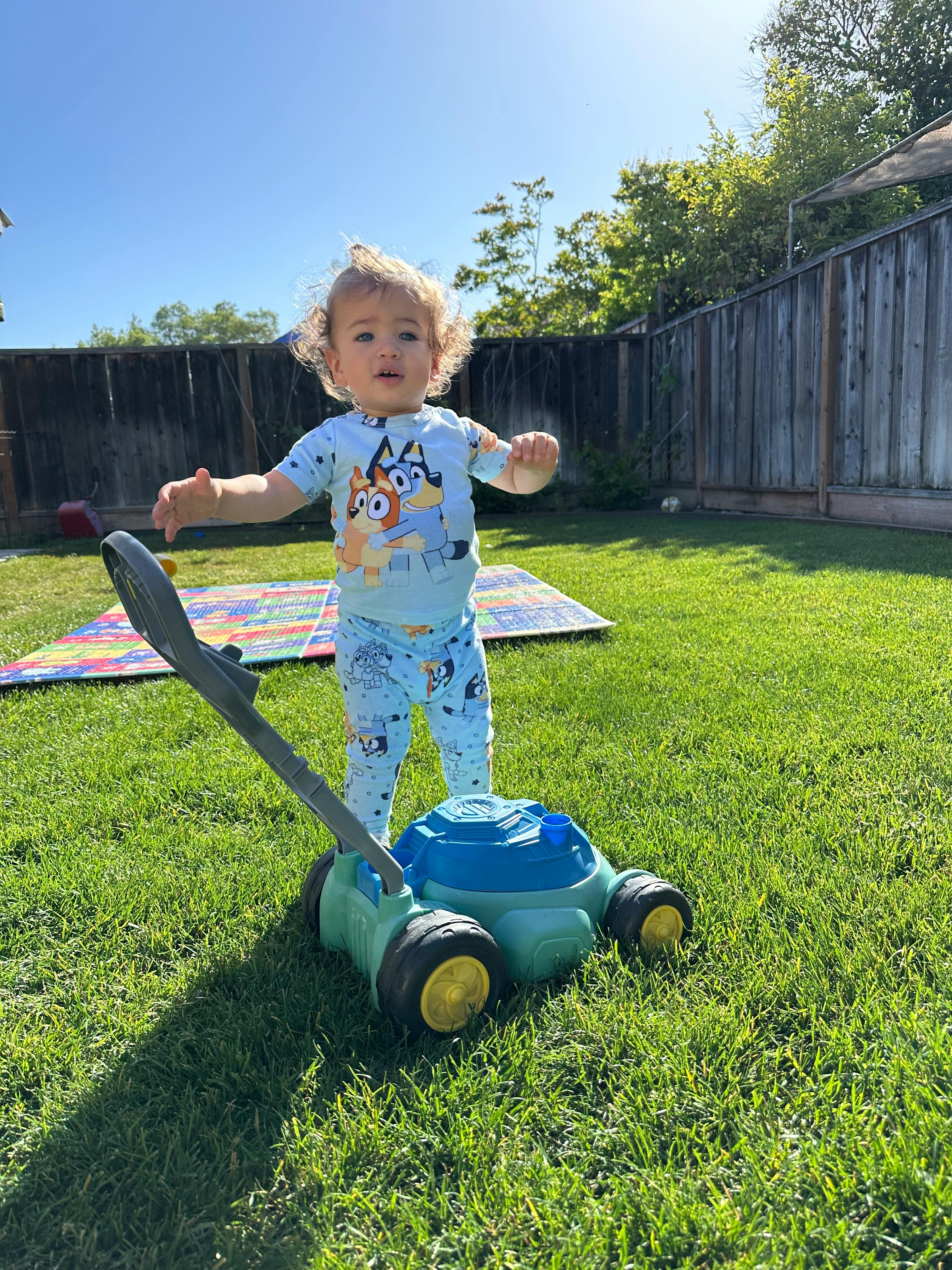 Child standing behind a toy lawnmower on grass
