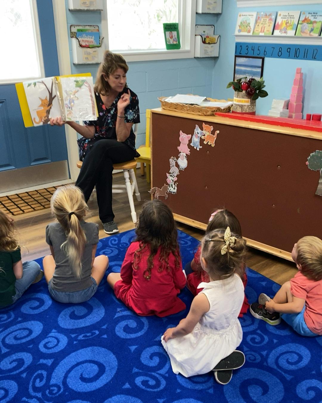 Person reading a book to children sitting on a rug in a classroom