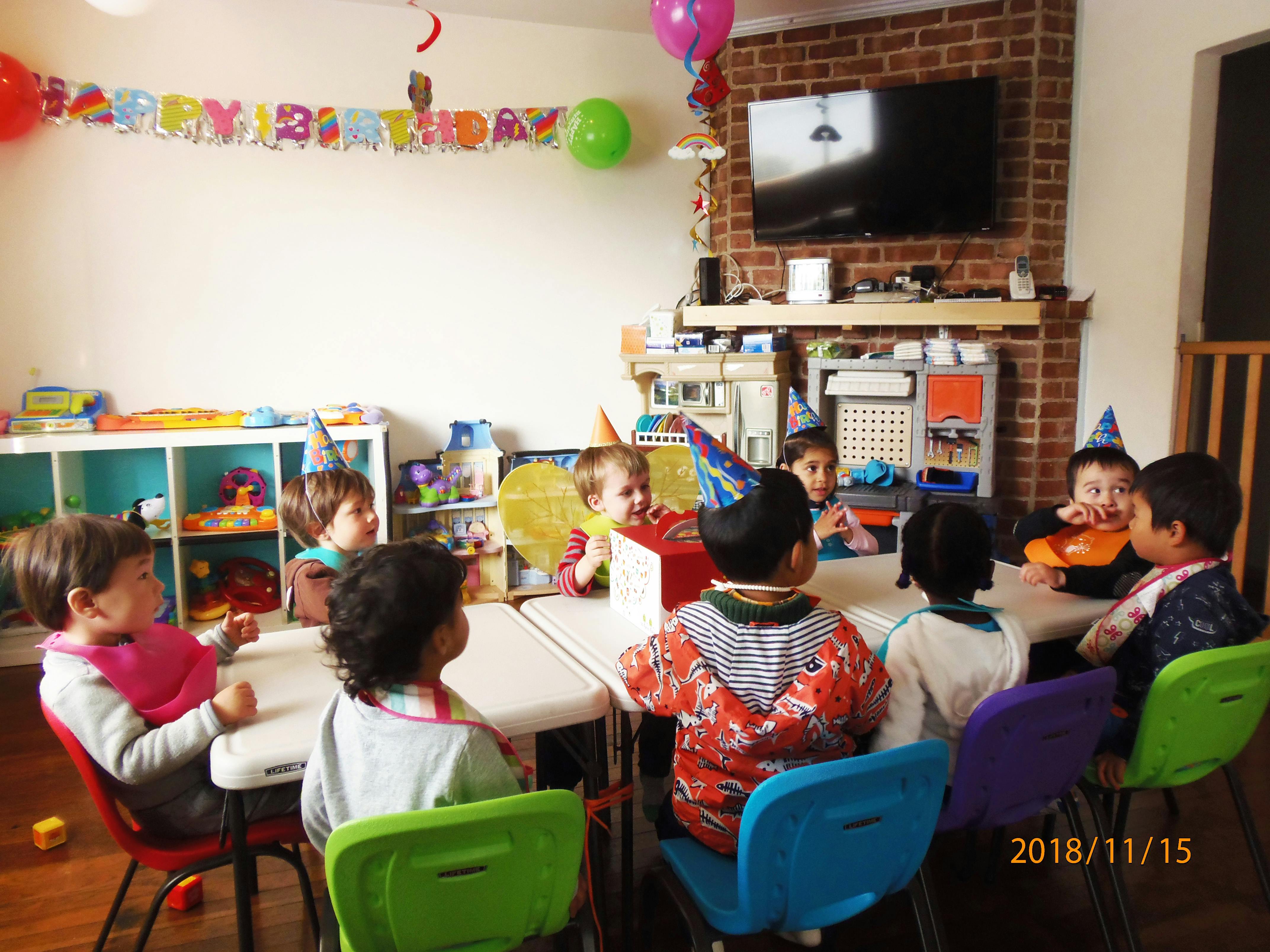 Children wearing party hats sitting around tables in a room with a "Happy Birthday" banner