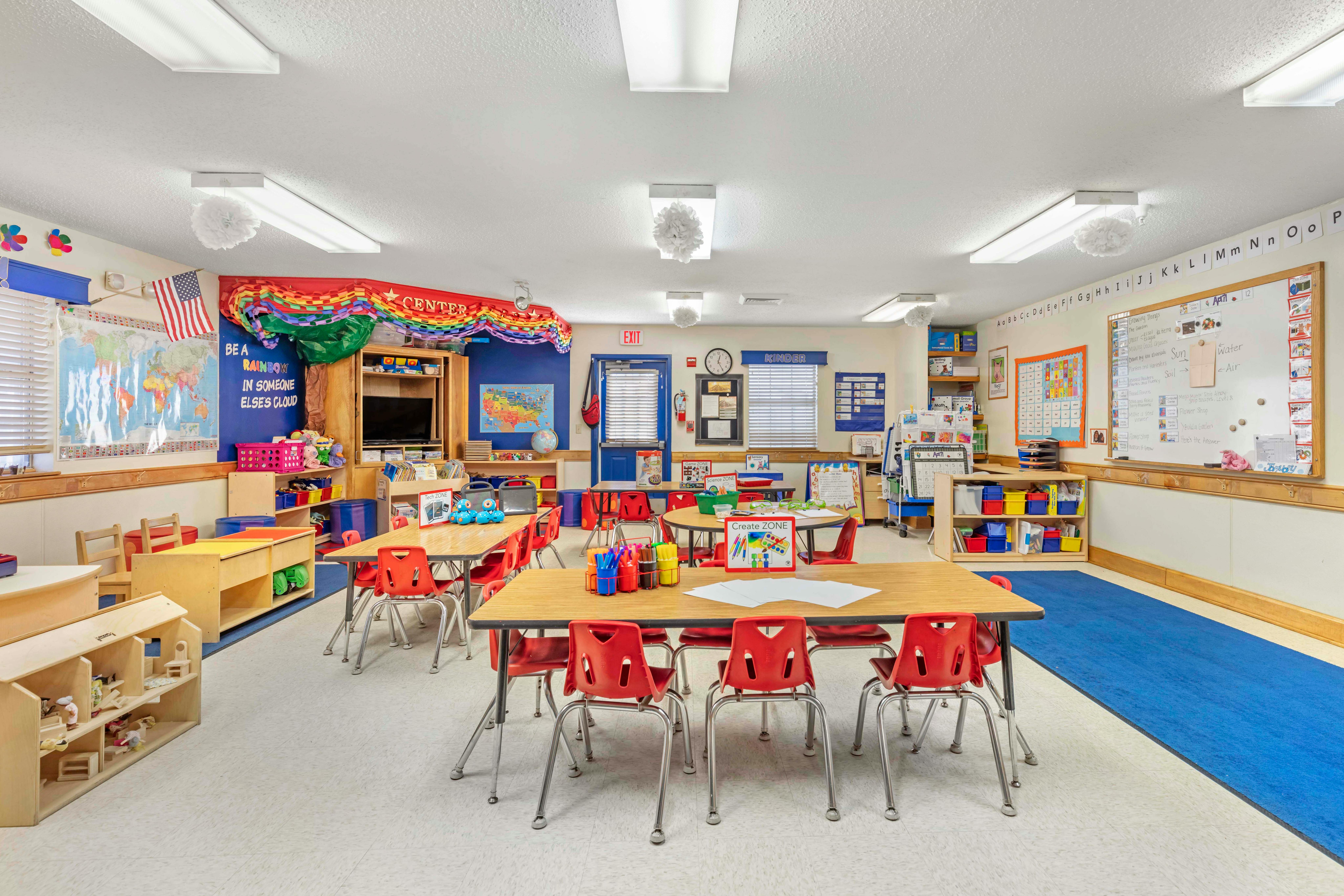 Classroom with small tables and red chairs, world map, and alphabet on the wall