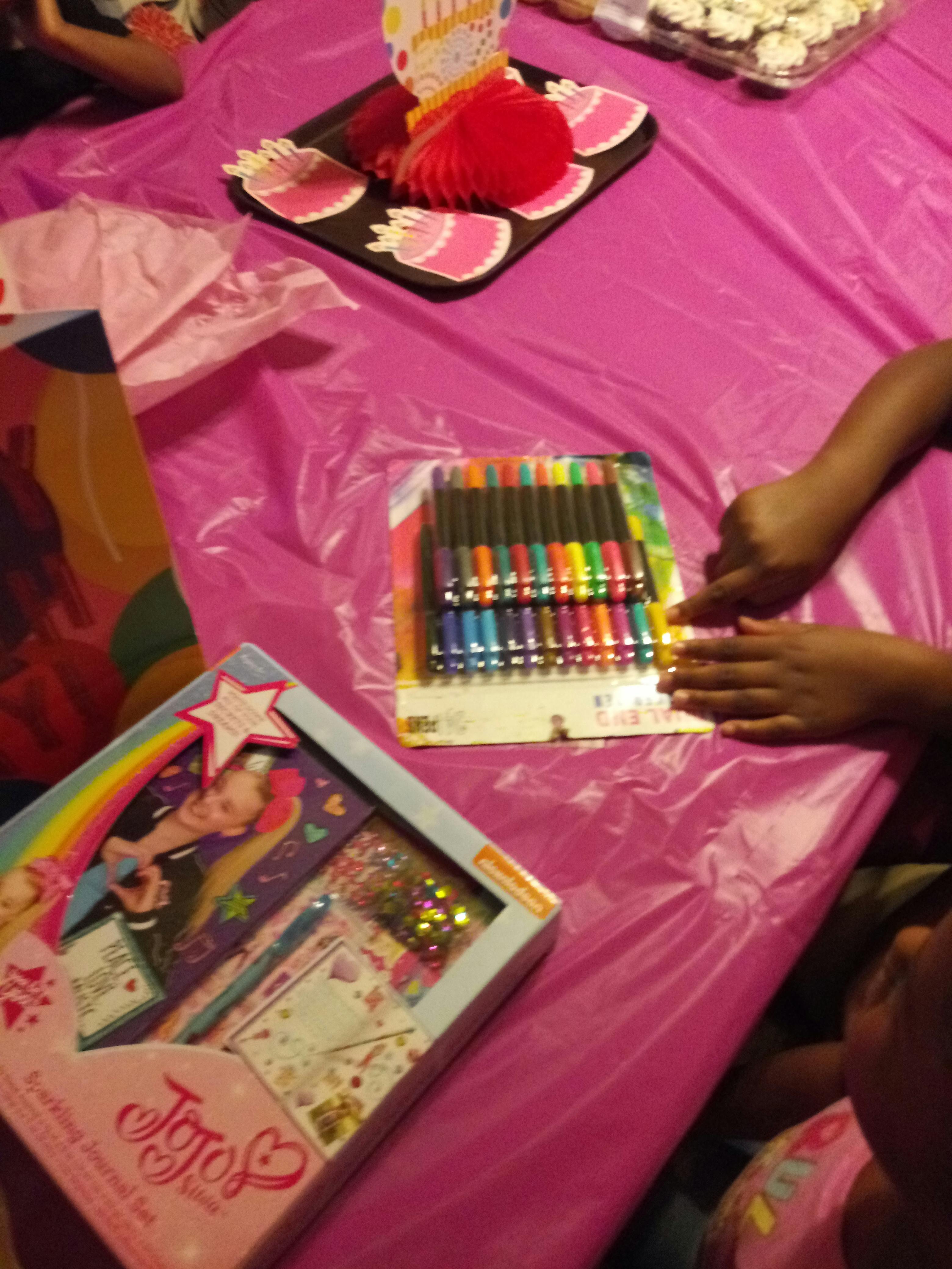 Hands reaching for a set of colorful pens on a pink table