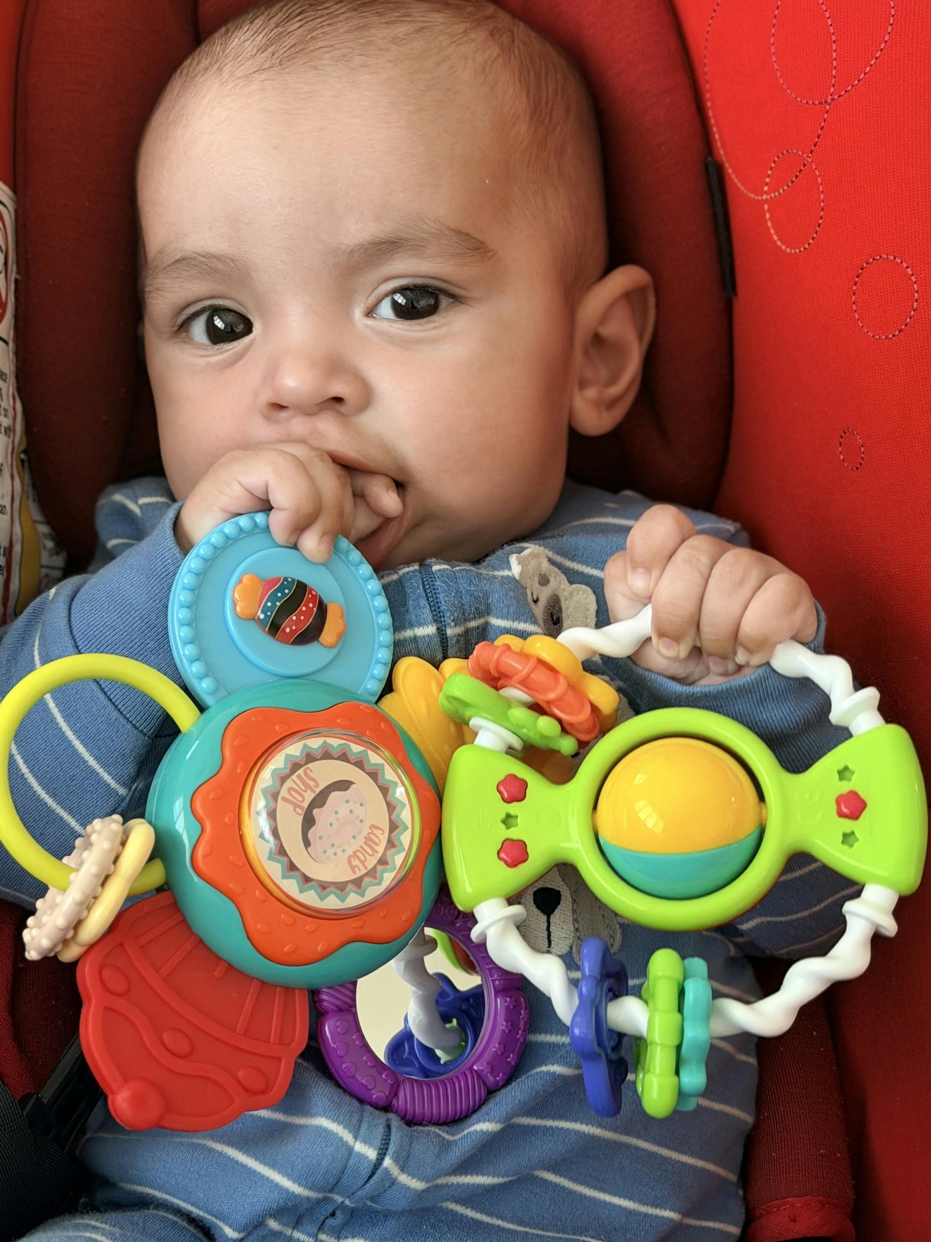 Child sitting in a car seat holding a colorful candy themed rattle