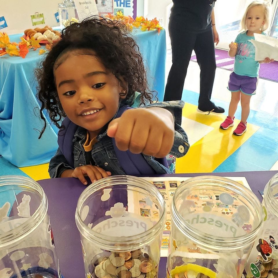 Child pointing forward with a fist, standing behind jars of jars of coins