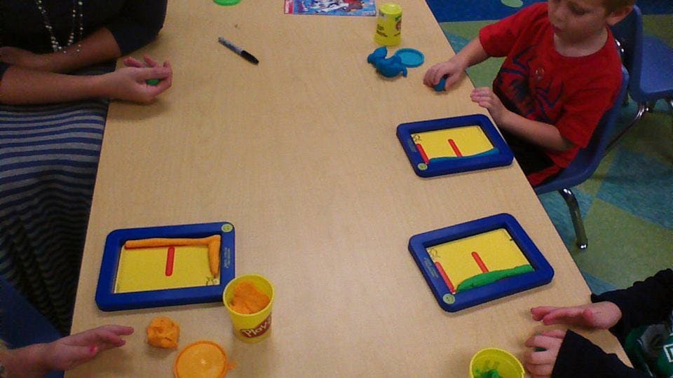 People and a child at a table with playdough and letter molds