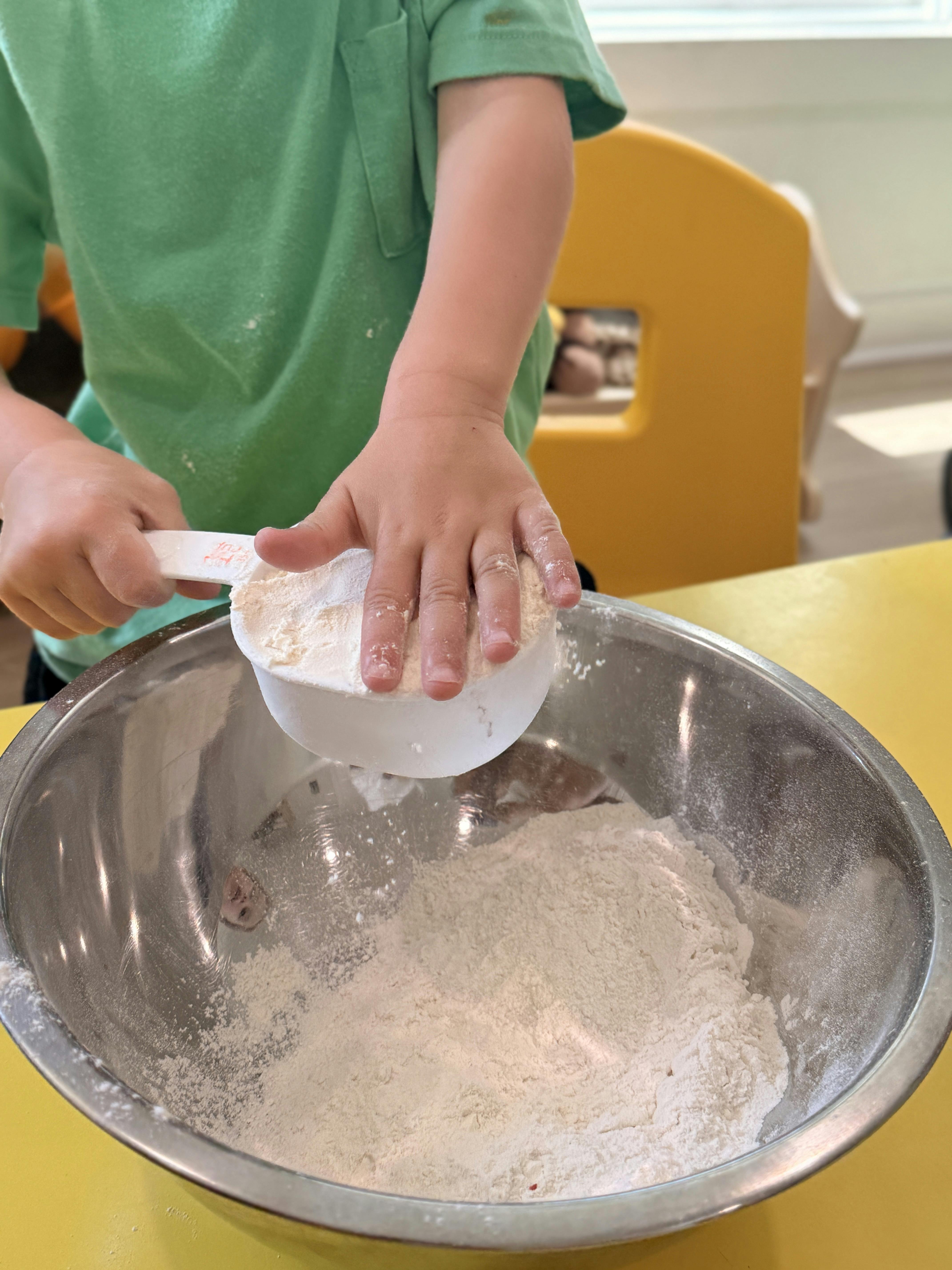 Child's hands scooping flour into a mixing bowl