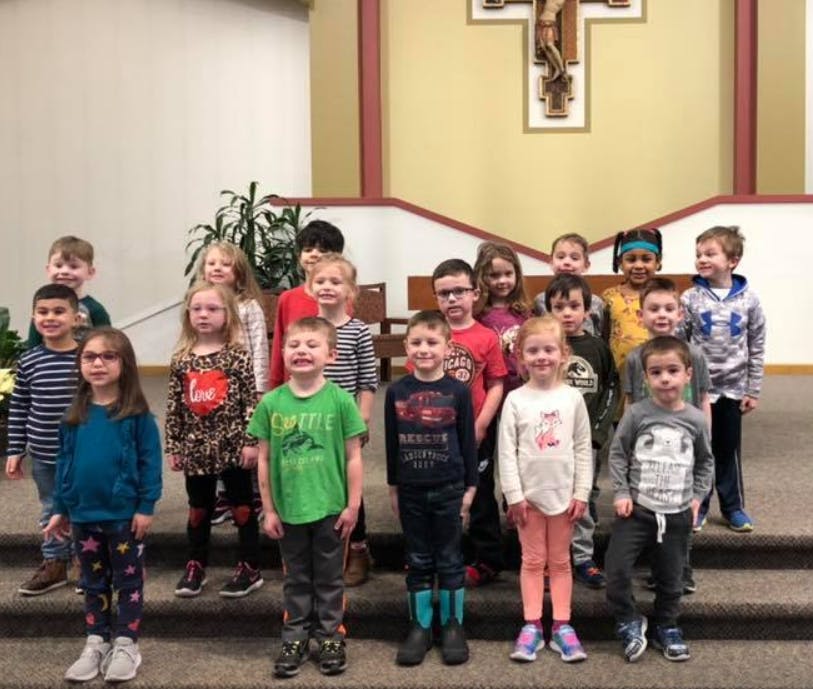 Group of children standing on steps in front of a crucifix