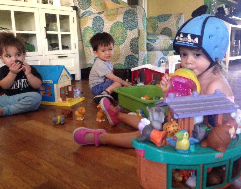 Three children playing with toys on a wooden floor