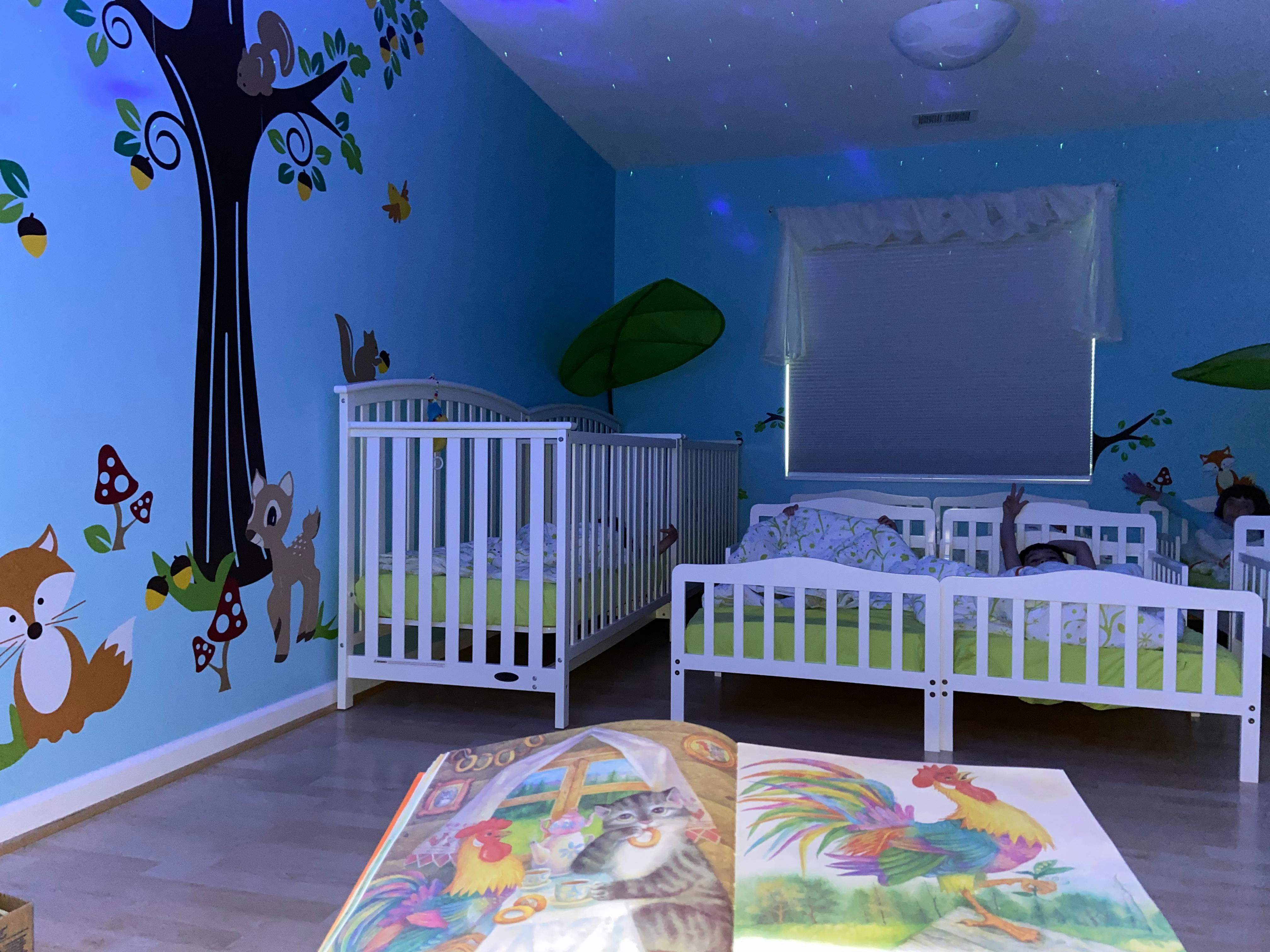 Nursery room with cribs and toddler beds, forest mural on wall