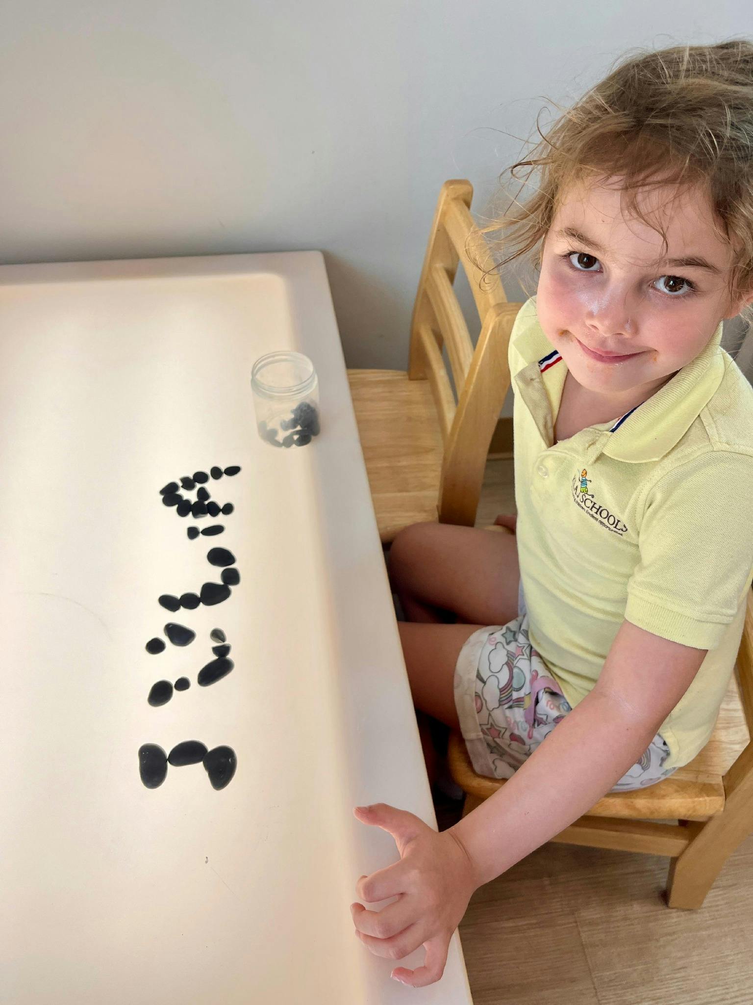 Child sitting at a table with small black objects arranged objects