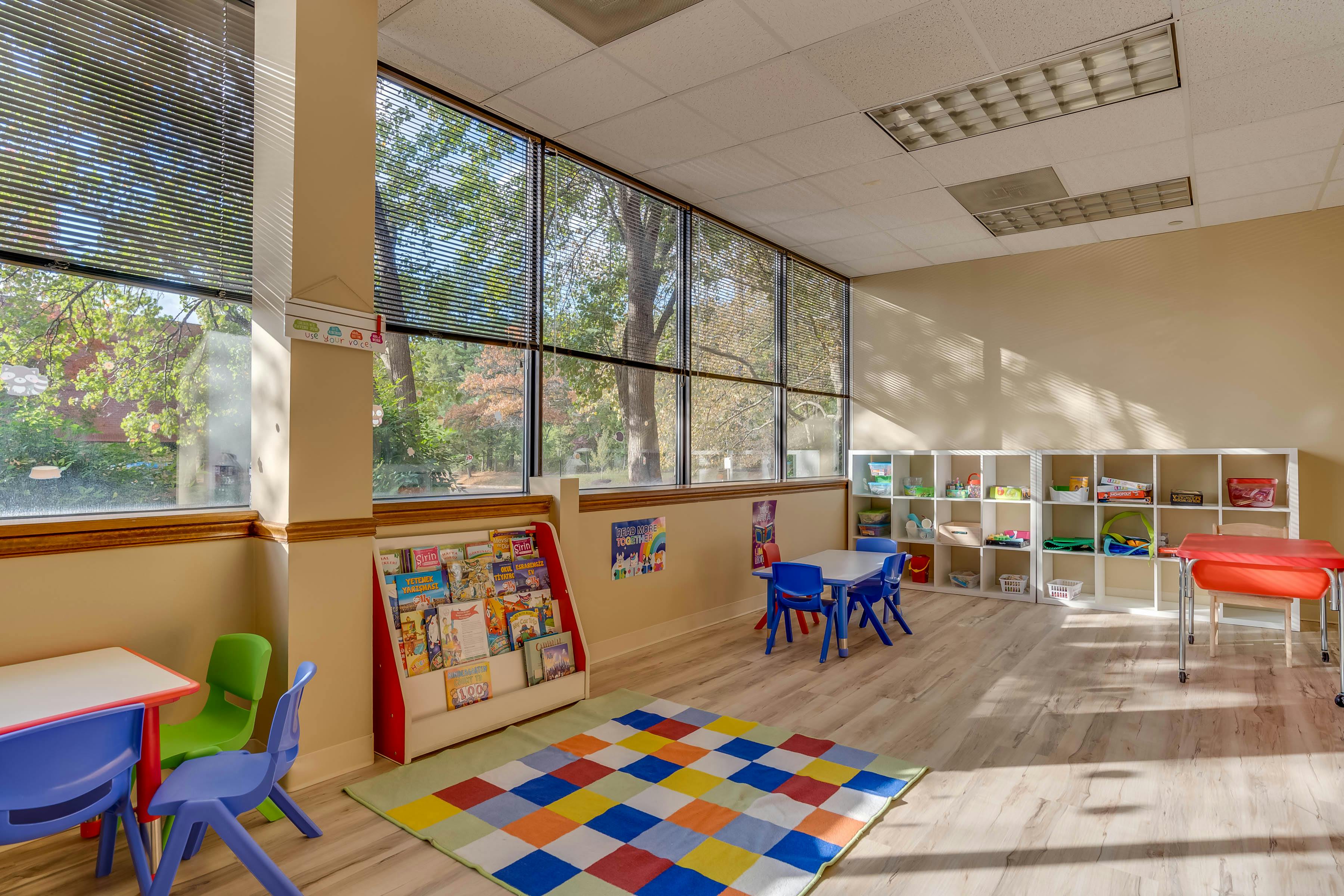 Classroom with small tables and chairs, a colorful rug, and large windows