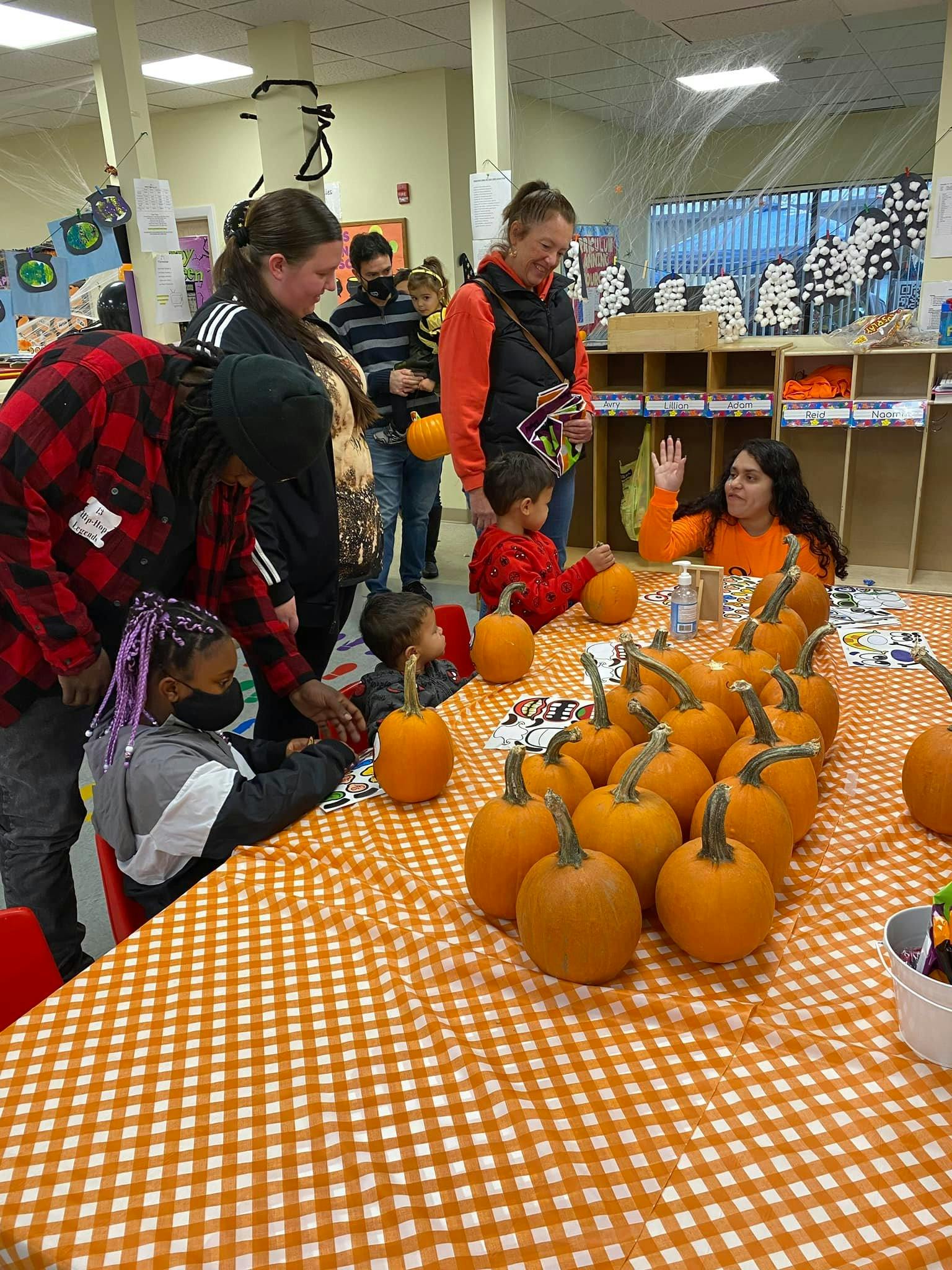People and children gathered around a table with many small pumpkins