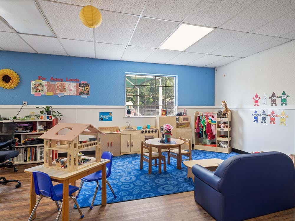 Playroom with dollhouse, blue rug, small tables, and toy kitchen