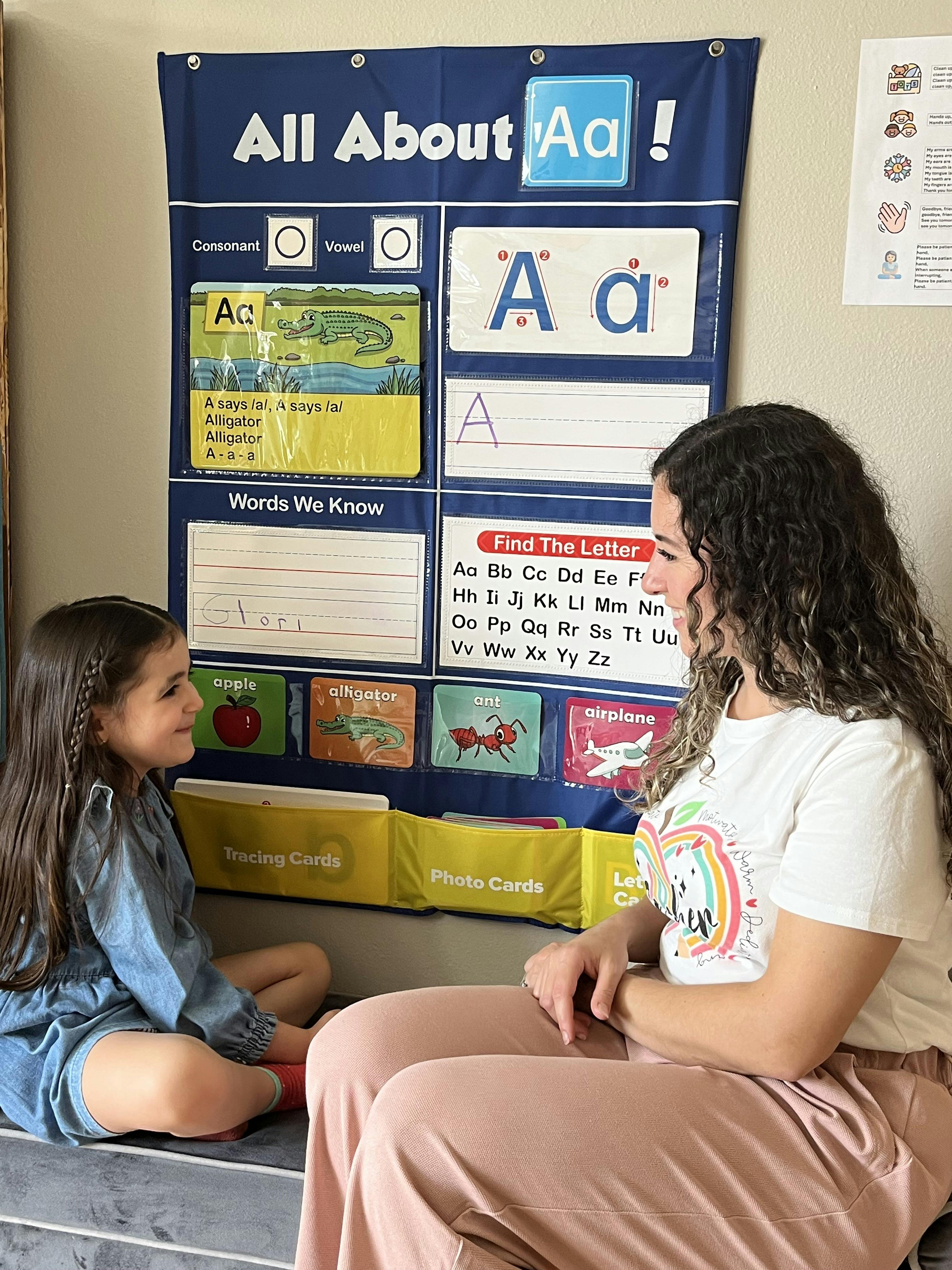 Adult and child sitting in front of an "All About Aa" learning chart