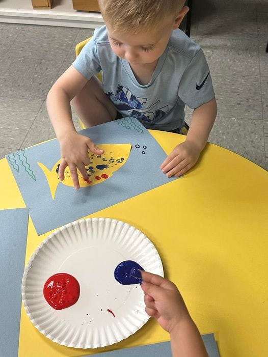 Child finger painting a fish cutout on blue paper