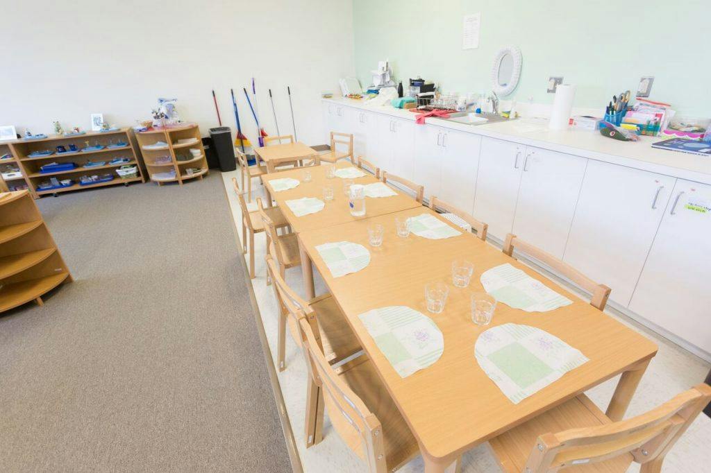 Classroom with long wooden tables and chairs, shelves, and counter space