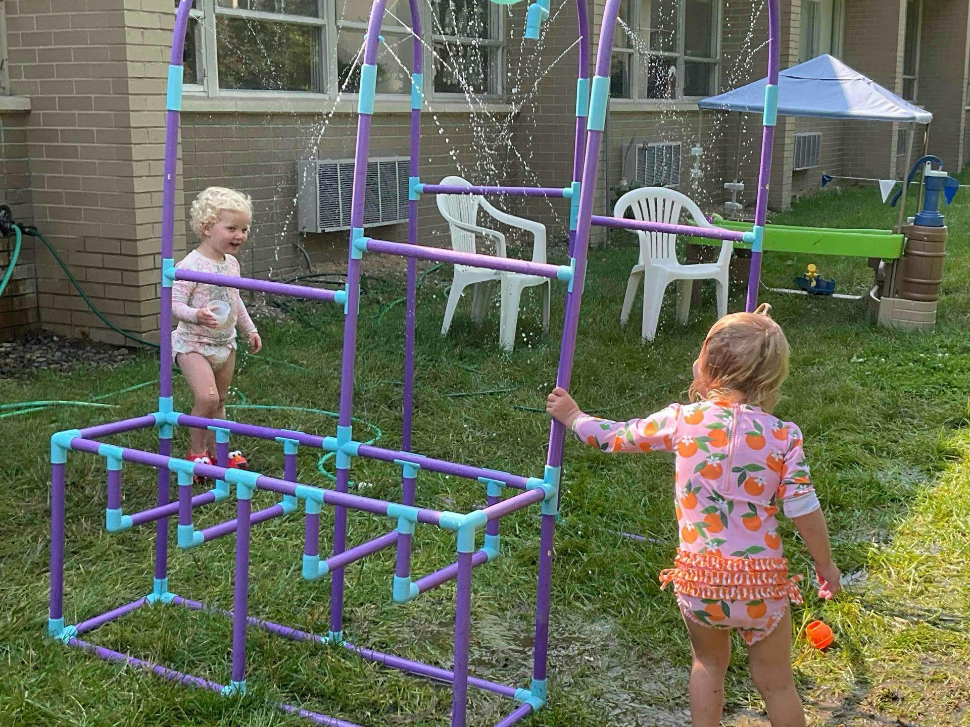Two children playing with a purple and blue PVC pipe structure outdoors