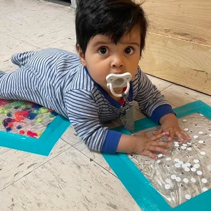 Child with pacifier on floor playing with sensory mats