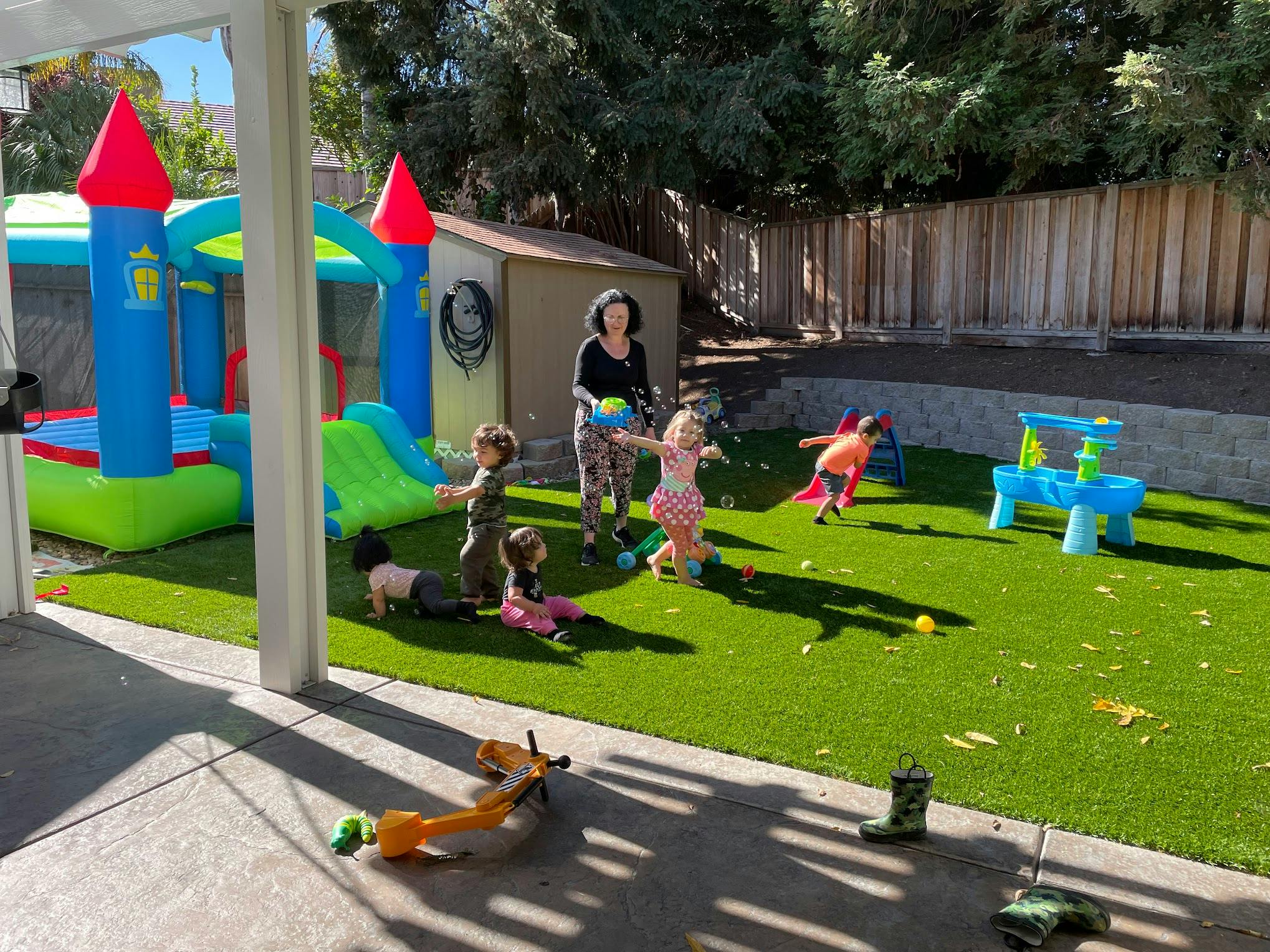 Adult blowing bubbles for children playing on artificial grass in a backyard