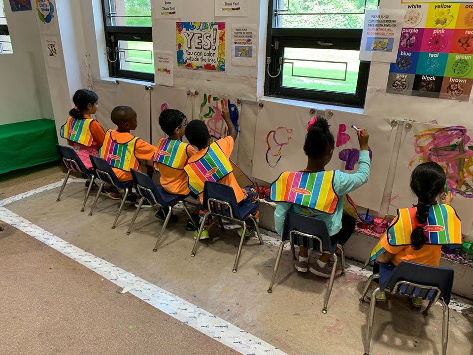 Children in vests painting at easels in a classroom